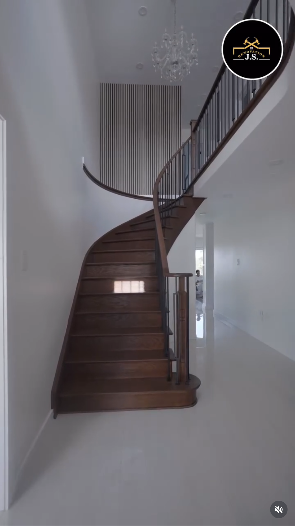 Interior view of a home with a curved wooden staircase featuring dark wood steps and black metal railing, leading to an upper floor with a chandelier hanging from the ceiling.