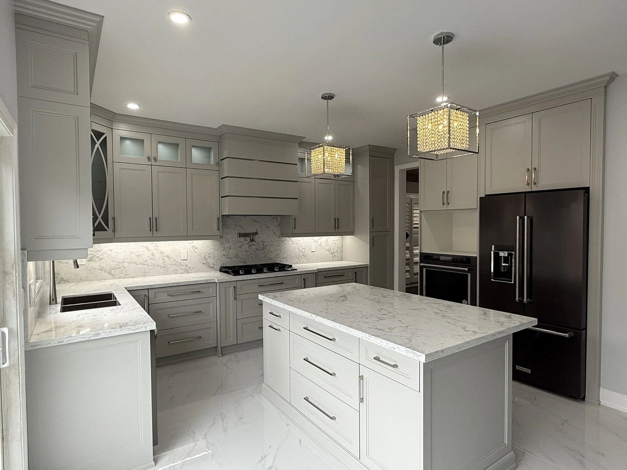Modern kitchen with gray cabinets, white marble countertops, a large island, and high-end appliances including a black refrigerator and oven.