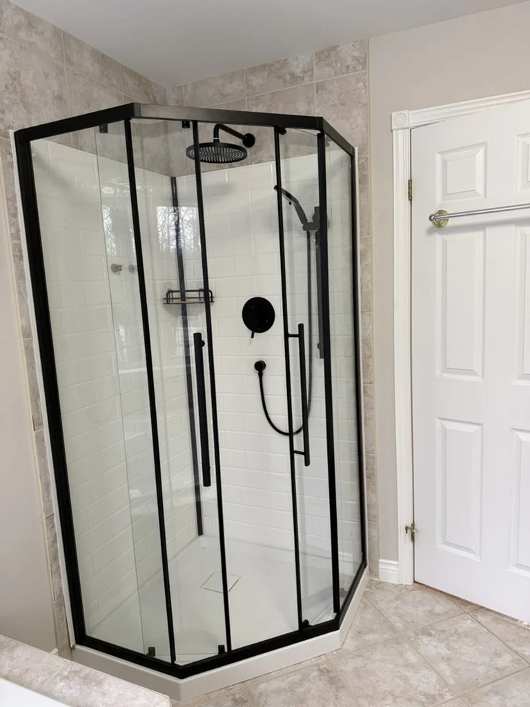 A modern corner shower with black metal framing, clear glass doors, and white subway tile walls.