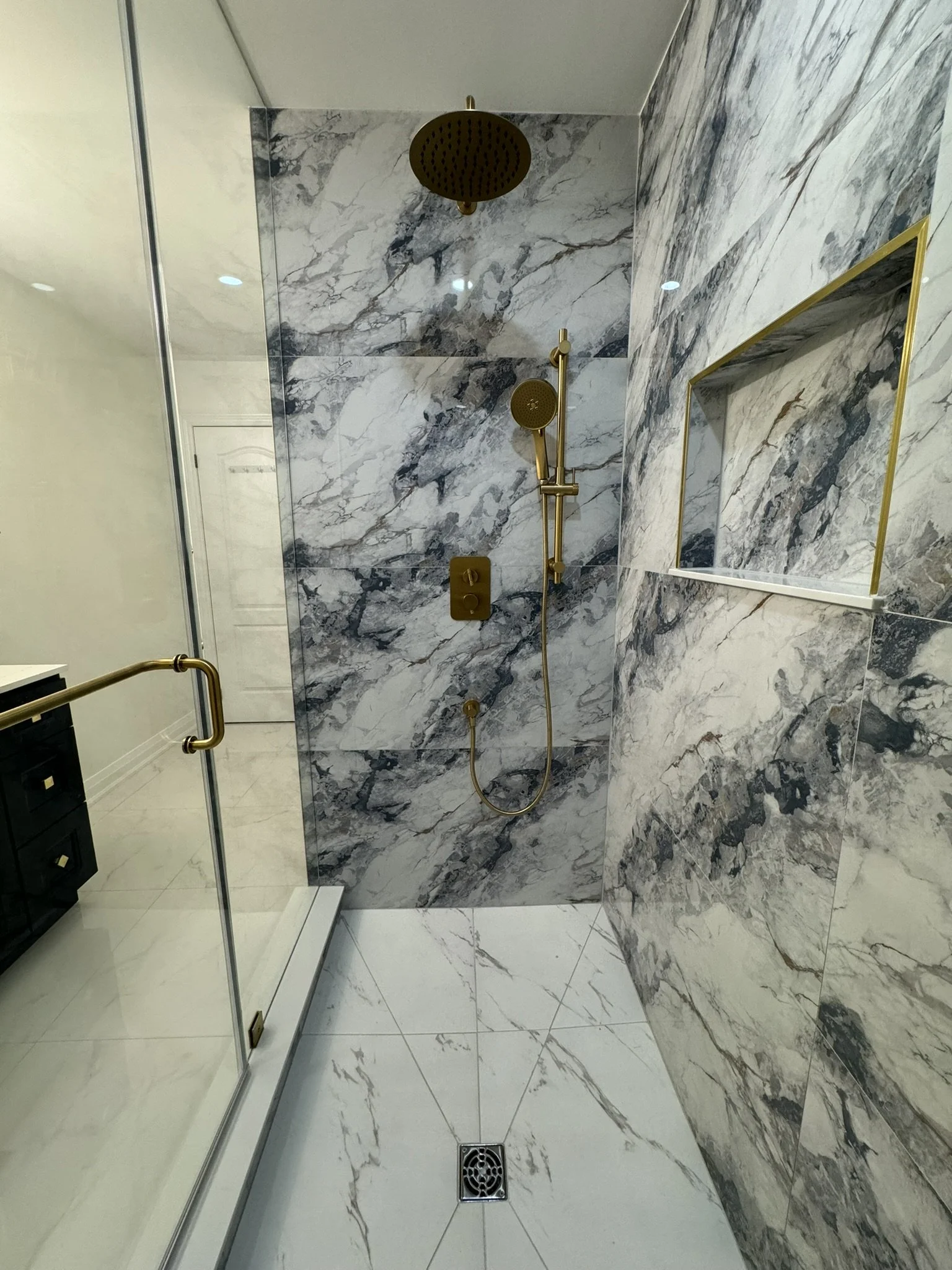 Modern shower with gold fixtures, marble walls, glass door, and a built-in niche