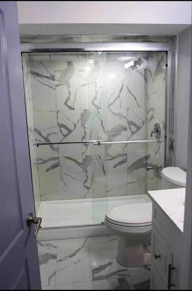 Small bathroom featuring a marble-tiled shower with glass doors, a white toilet, and a white vanity with a marble countertop.