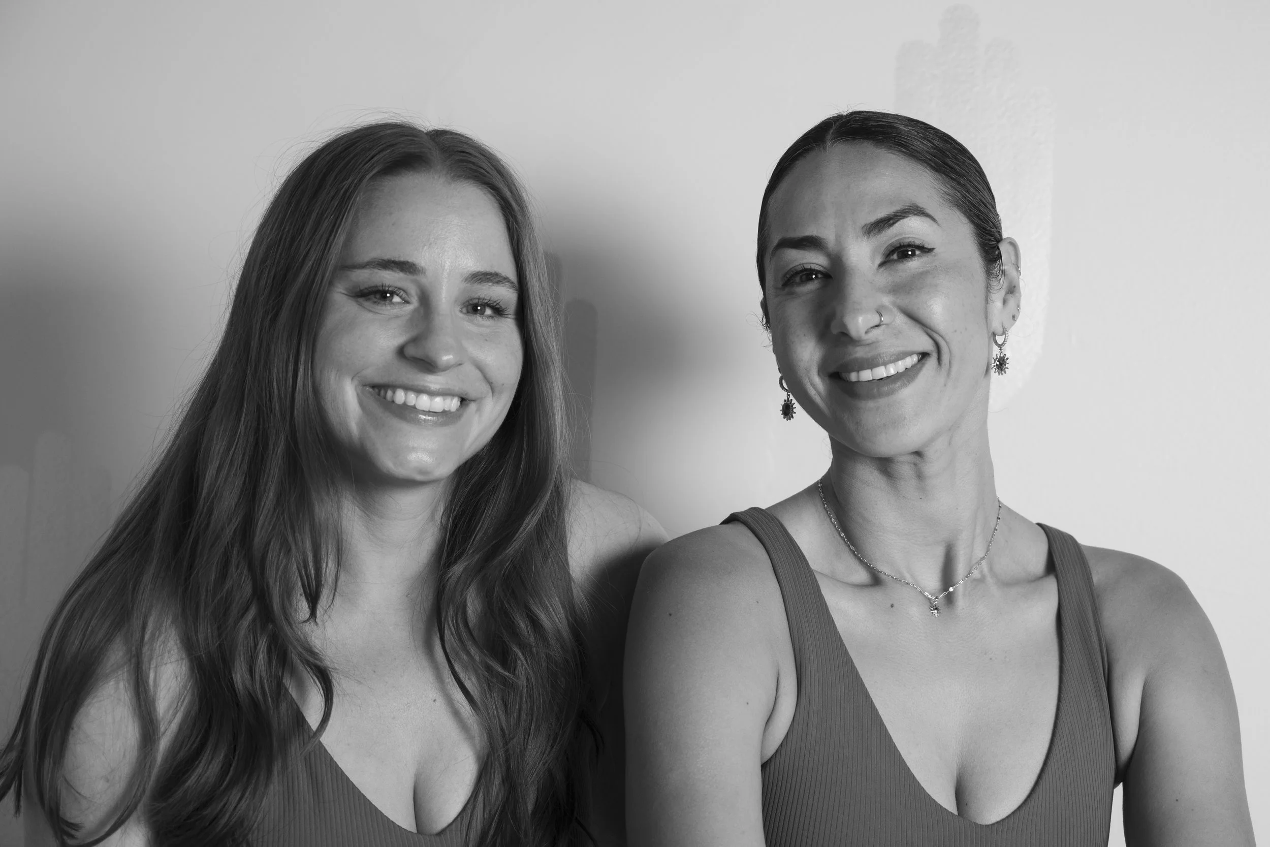 Two women smiling in black and white, standing close to each other against a plain background.