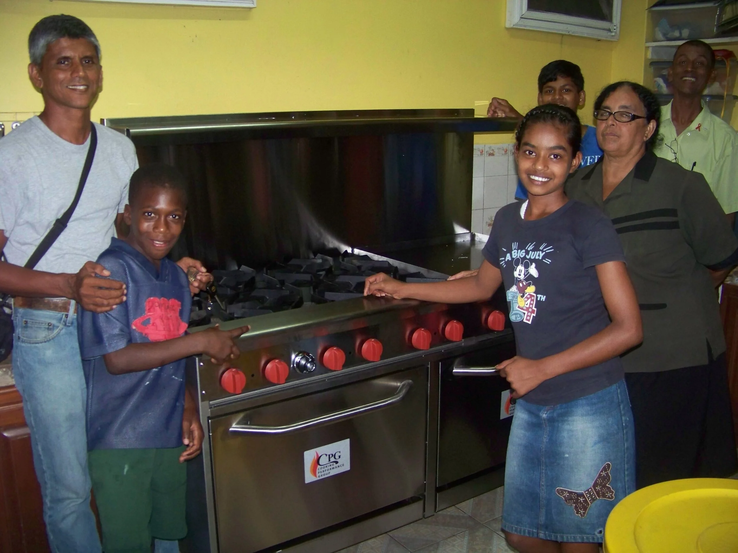 Group of six people, including children and adults, gathered around a new stove in a kitchen, smiling and posing for the camera.