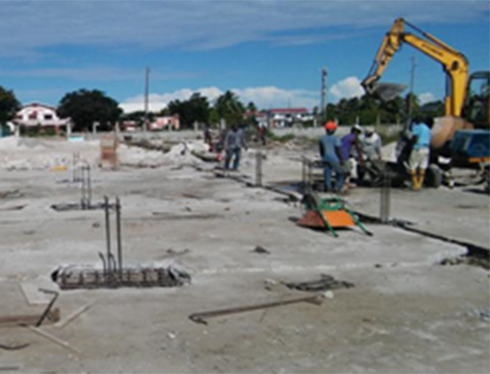 Construction site with workers and a yellow excavator working on a concrete foundation.