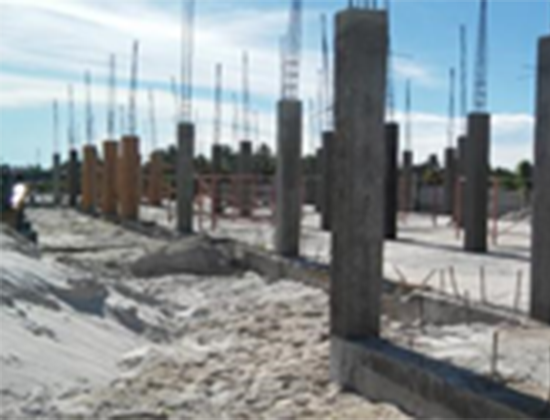Construction site with vertical concrete pillars and blue safety netting overhead.