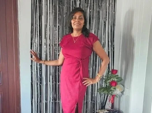 A woman standing in front of a black and white striped curtain, wearing a pink dress and smiling.