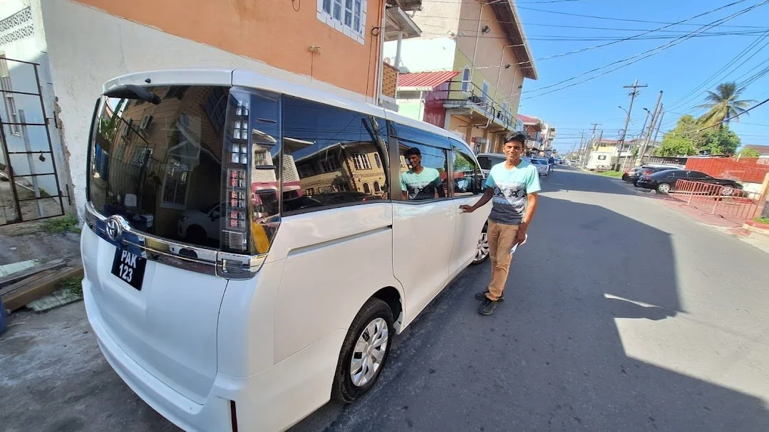 A person standing next to a white van on a city street with residential buildings, power lines, and a clear blue sky in the background.