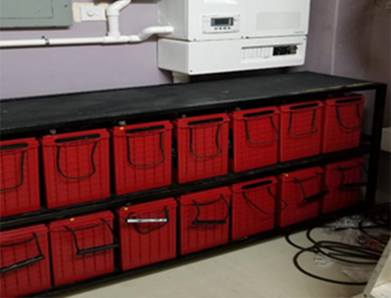 A black metal shelf with two rows of red storage bins, six in each row, in a room with a white wall and a white device above.