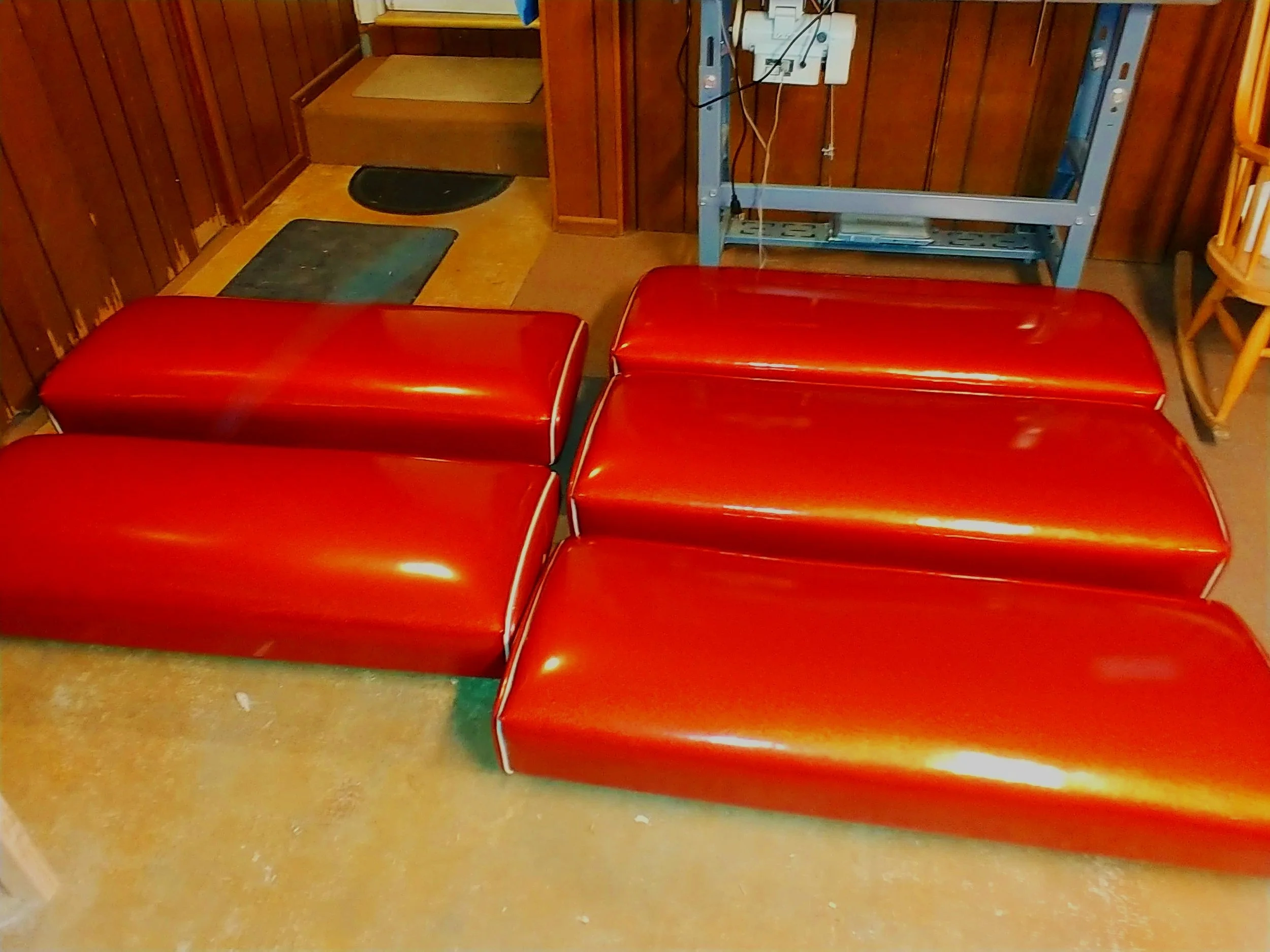 Four red rectangular cushions with rounded edges placed on a tan carpeted floor in a room with wood-paneled walls.