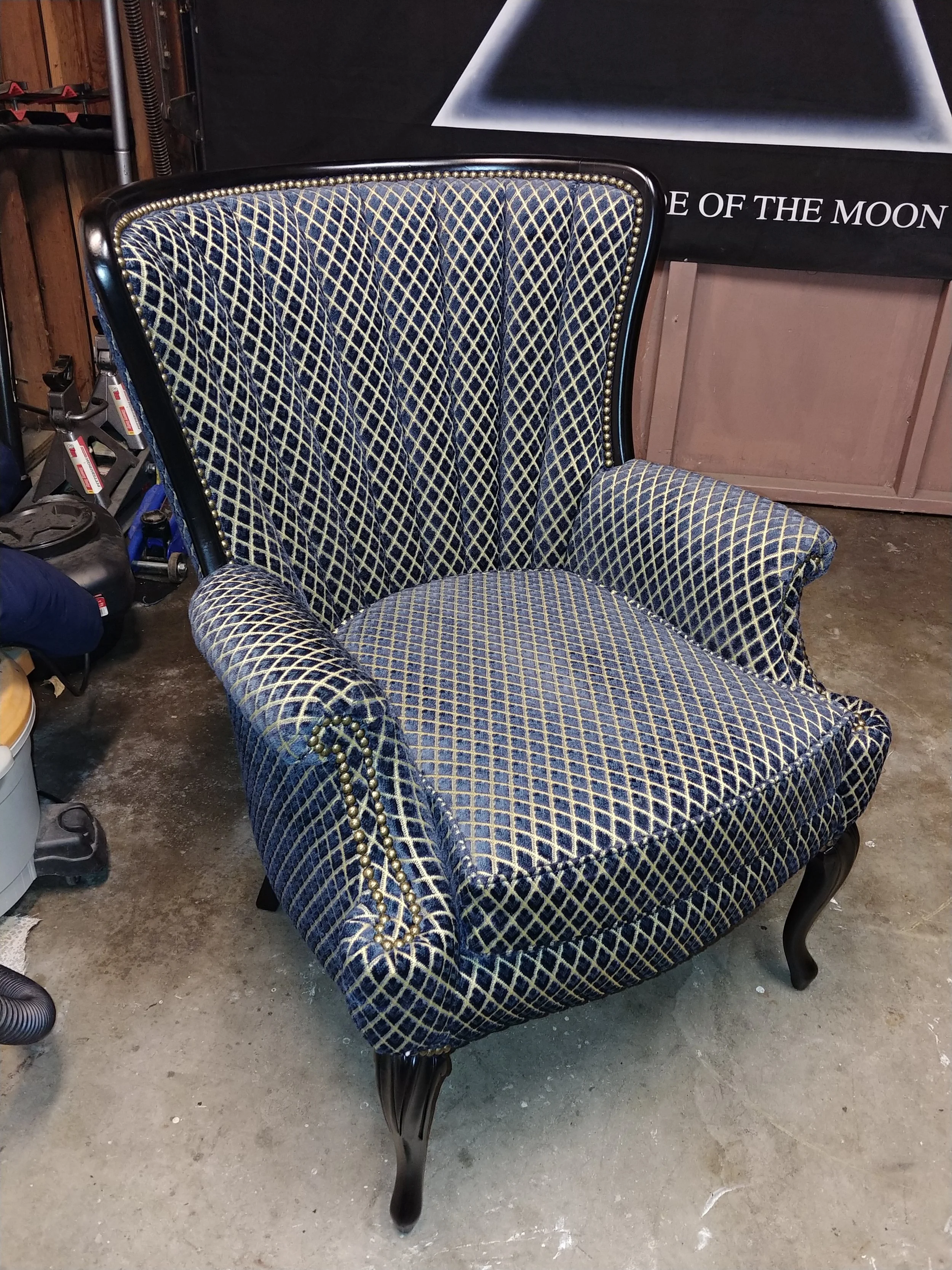 Vintage upholstered armchair with blue and gold diamond-patterned fabric and dark wooden legs, placed on a concrete floor in a garage or storage area.