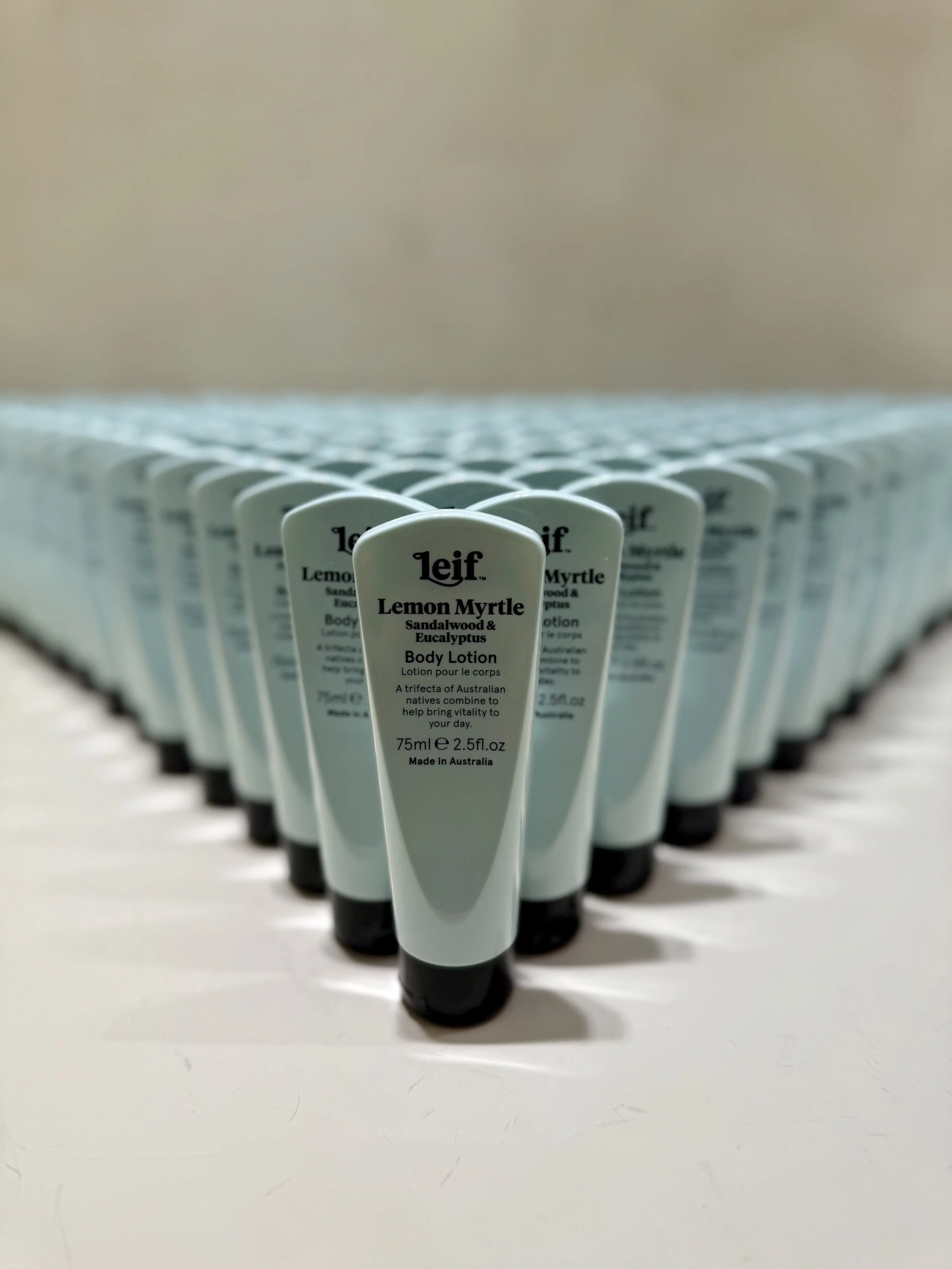Multiple bottles of Leif Lemon Myrtle body lotion arranged in a line on a white surface.