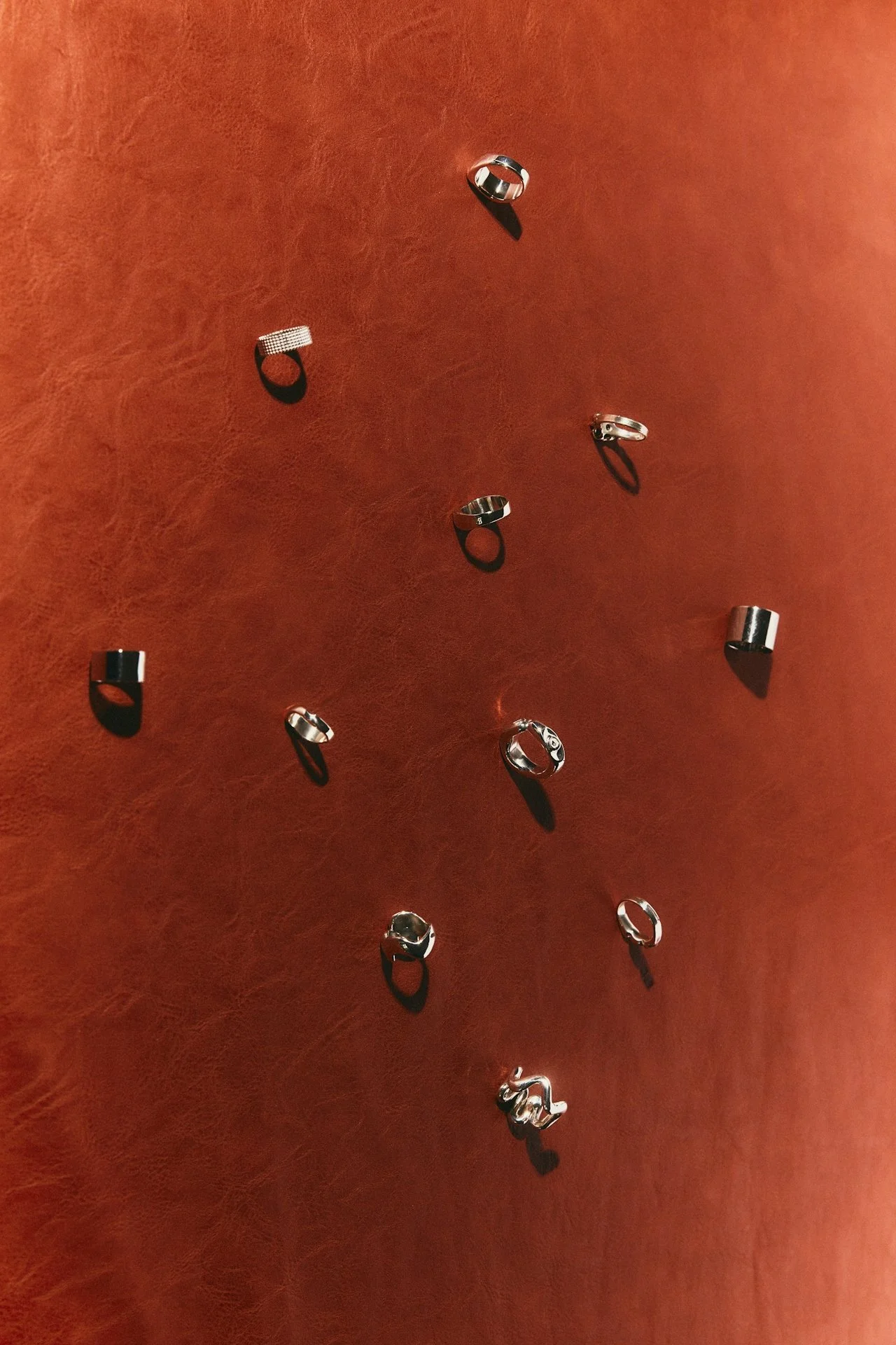 Multiple silver rings and a keychain on a brown textured surface.