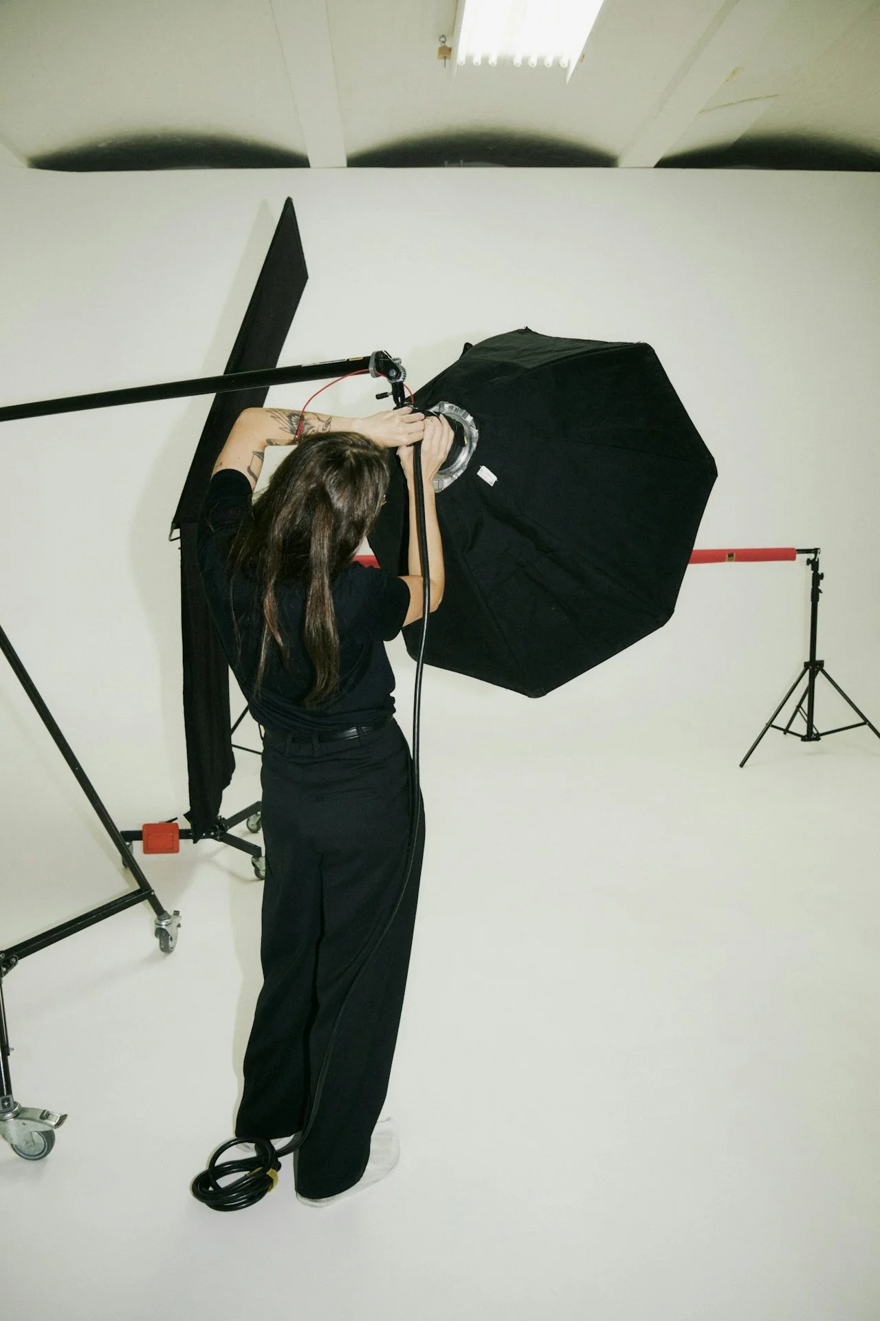 Woman adjusting a photography studio umbrella light on a white background.