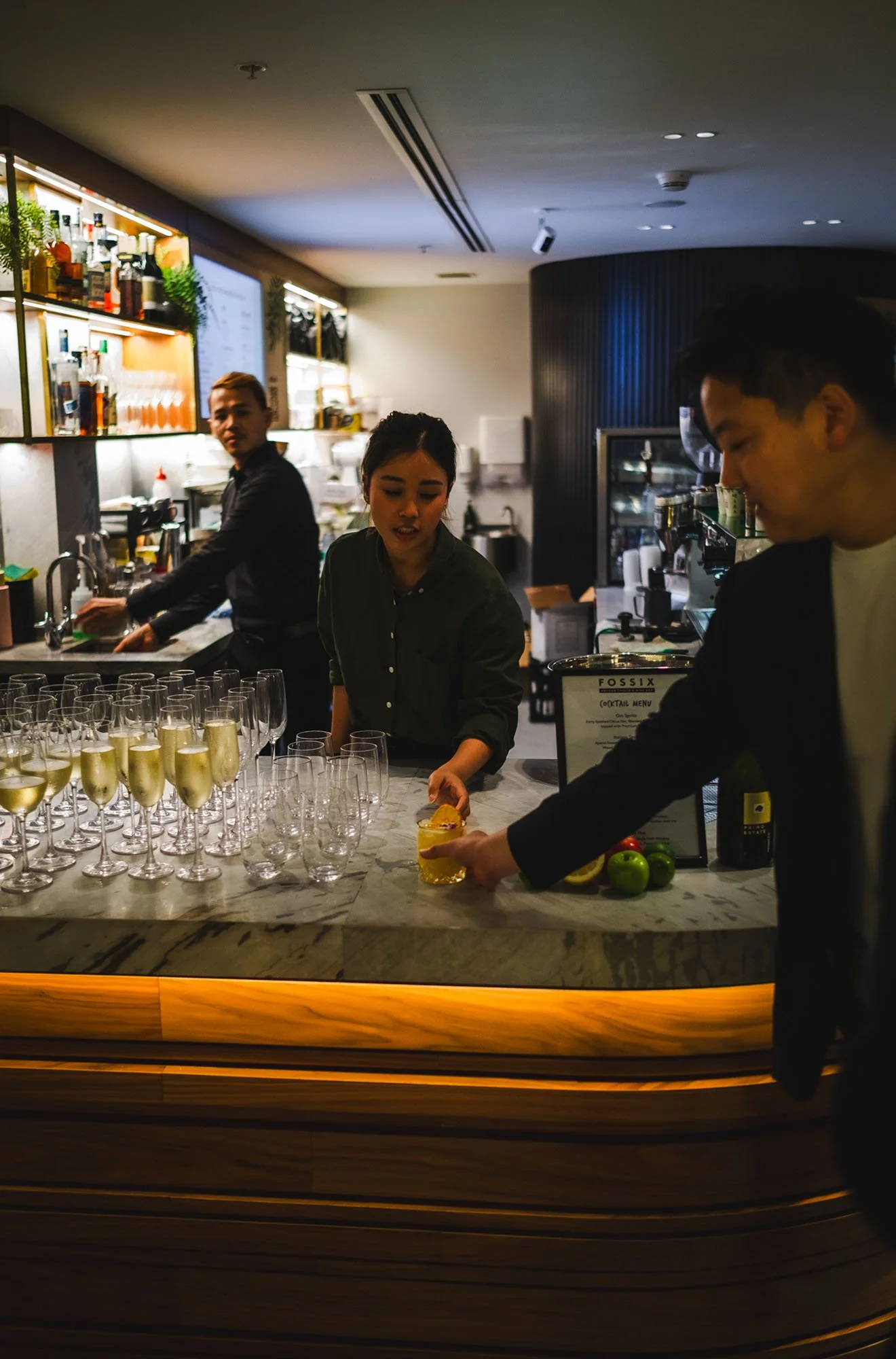 Bar staff preparing drinks behind a marble counter, with glasses of champagne, in a modern bar setting.