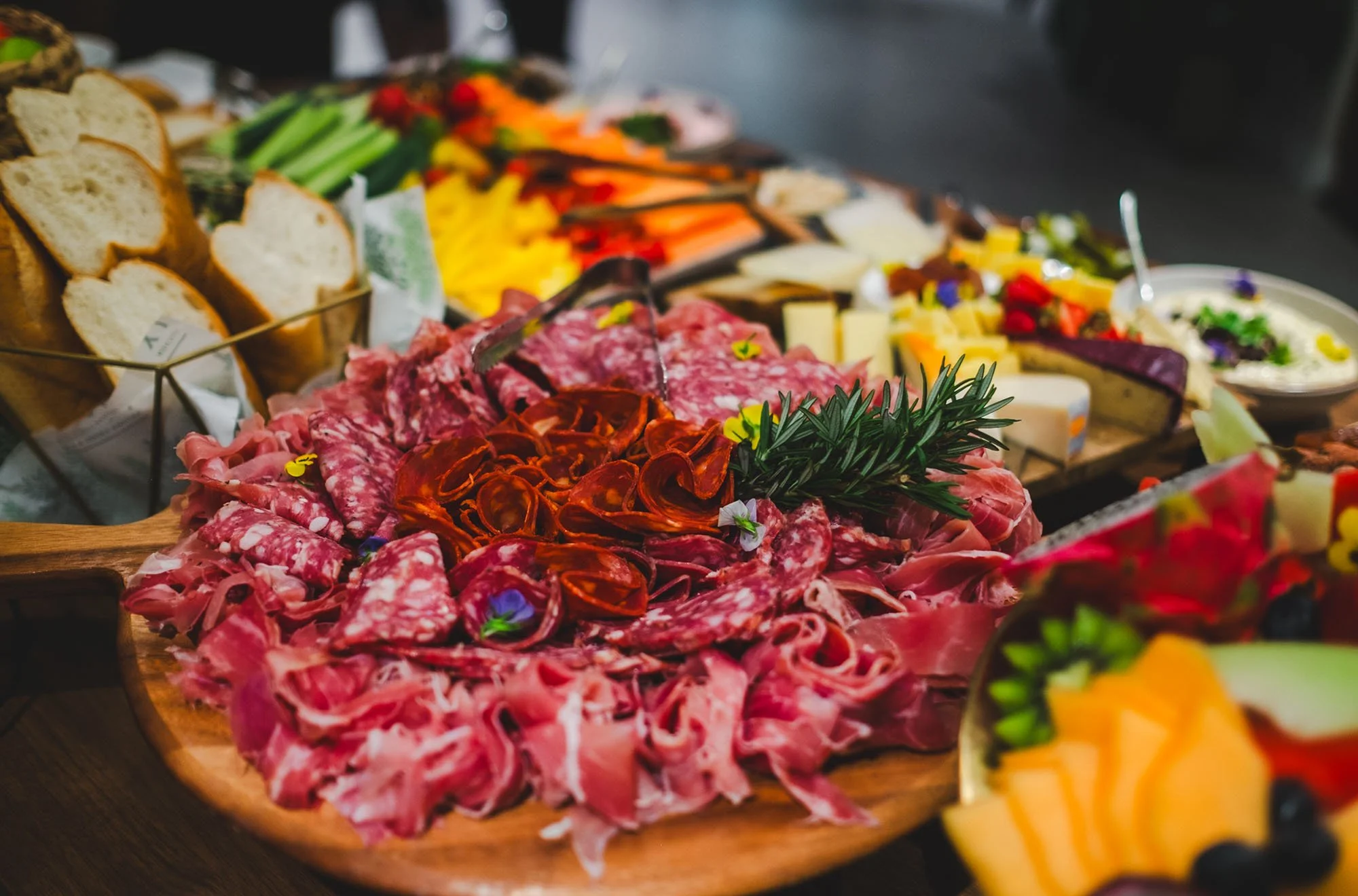 Assorted cured meats, cheeses, bread, and vegetables on a table for a charcuterie board.