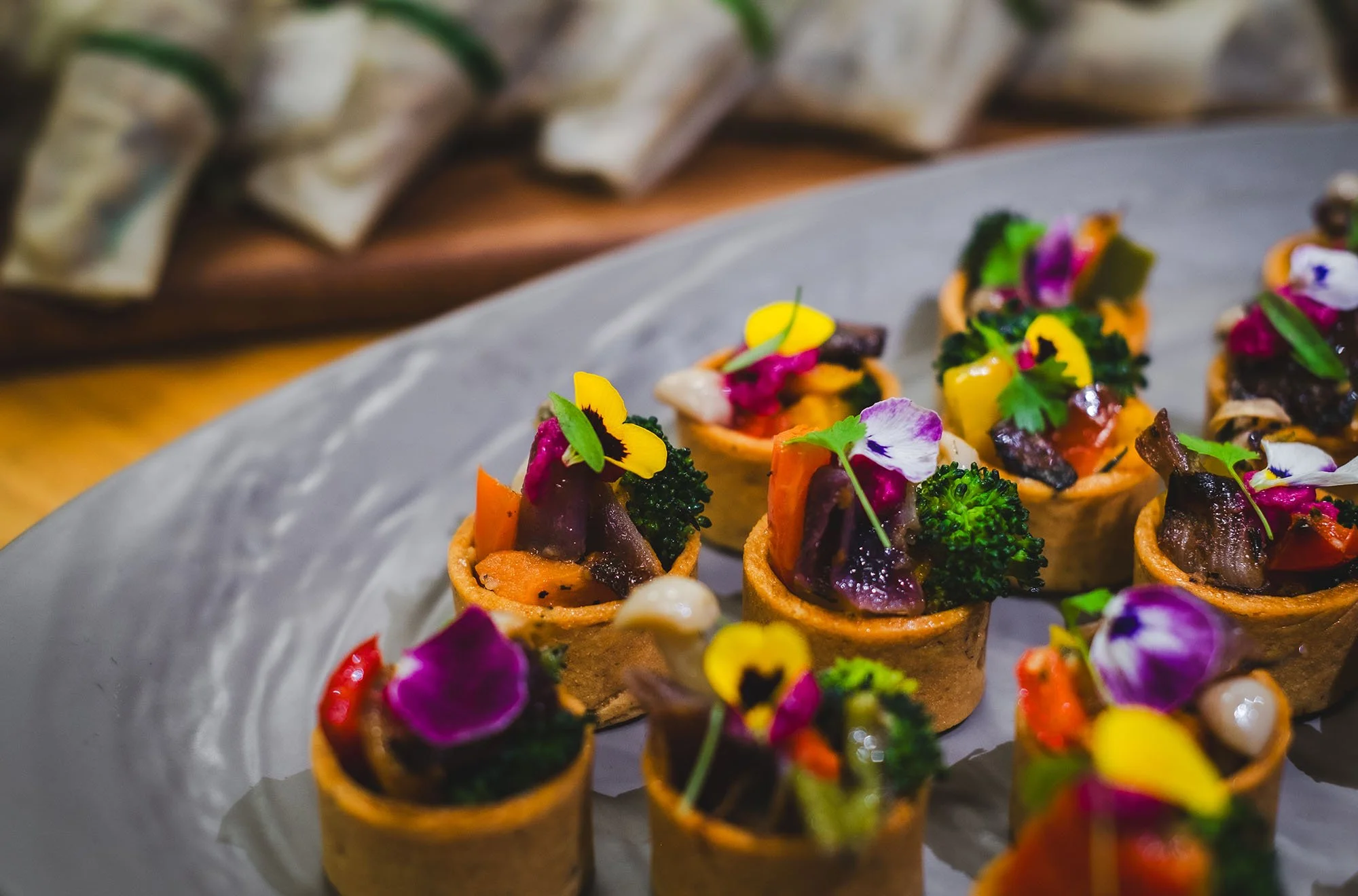 Miniature savory tartlets filled with vegetables, decorated with edible flowers on a platter.