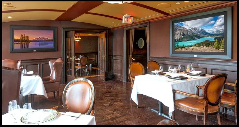 Elegant restaurant dining room with white tablecloths, leather chairs, and large landscape paintings on dark wood-paneled walls