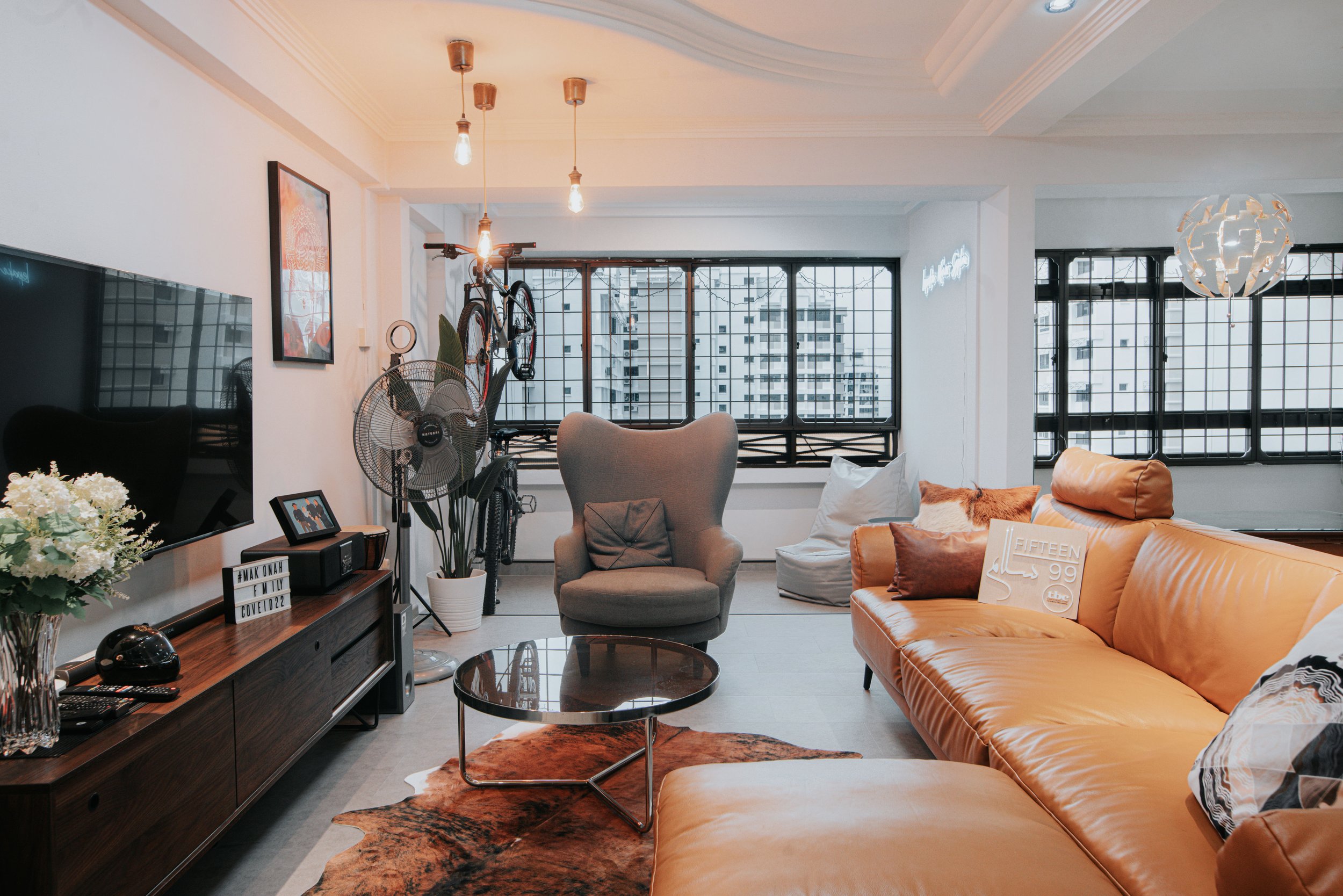 Spacious living room with a tan leather sofa and a round coffee table, featuring large windows and stylish decor.