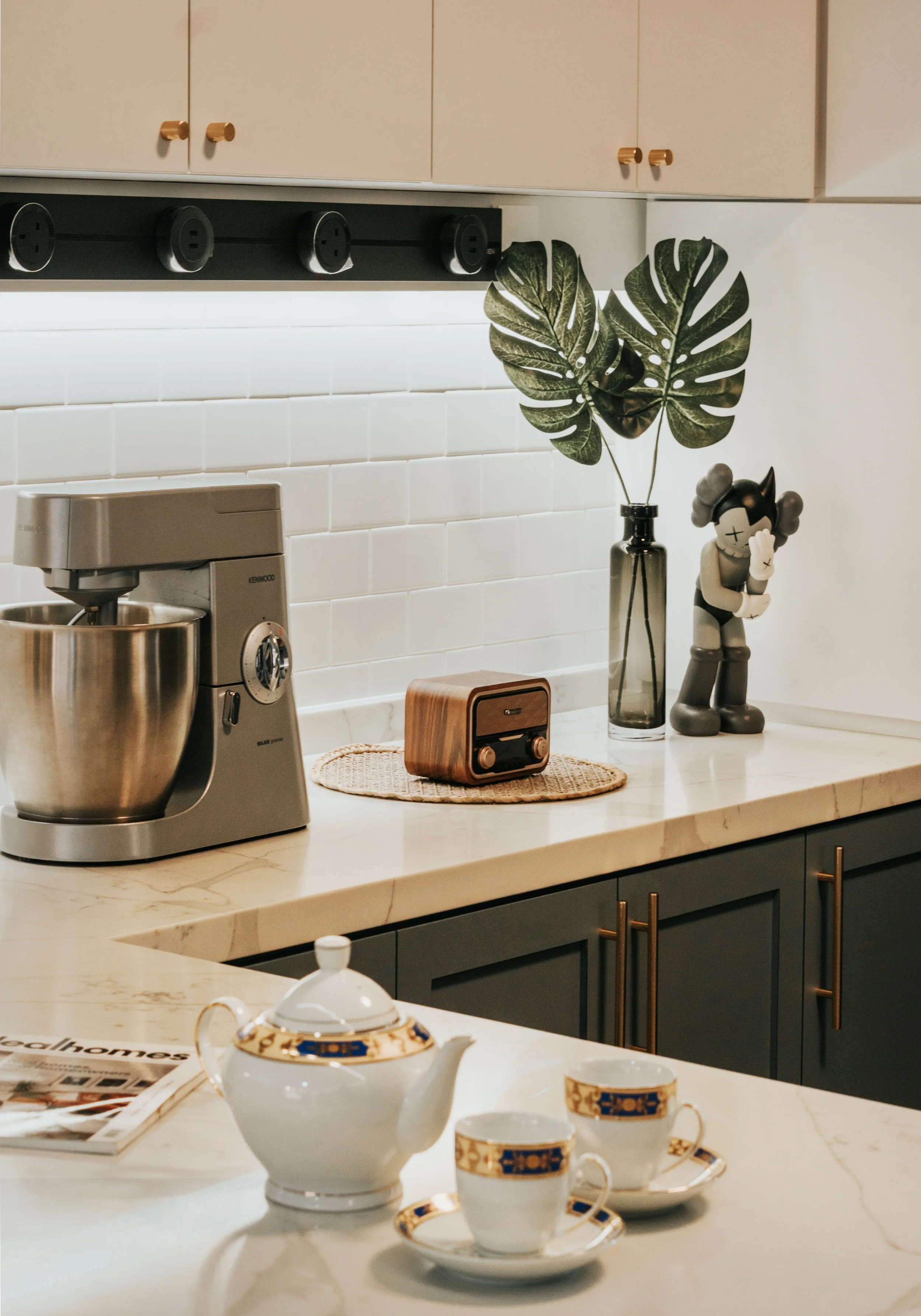 A modern kitchen counter featuring a stand mixer, decorative plants, and vintage radio with teapot and cups.