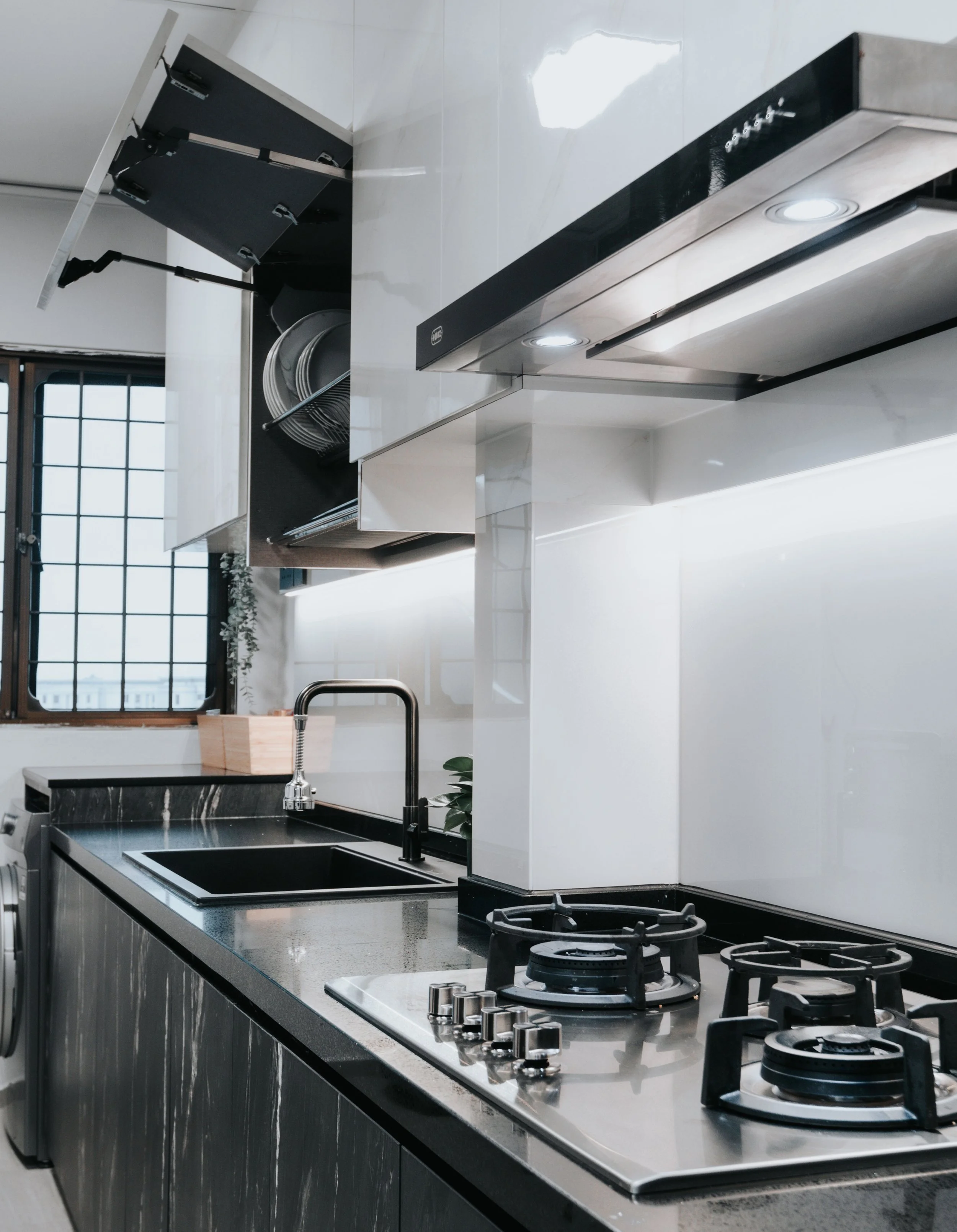 Sleek modern kitchen with black countertops, stainless steel appliances, and a large window.