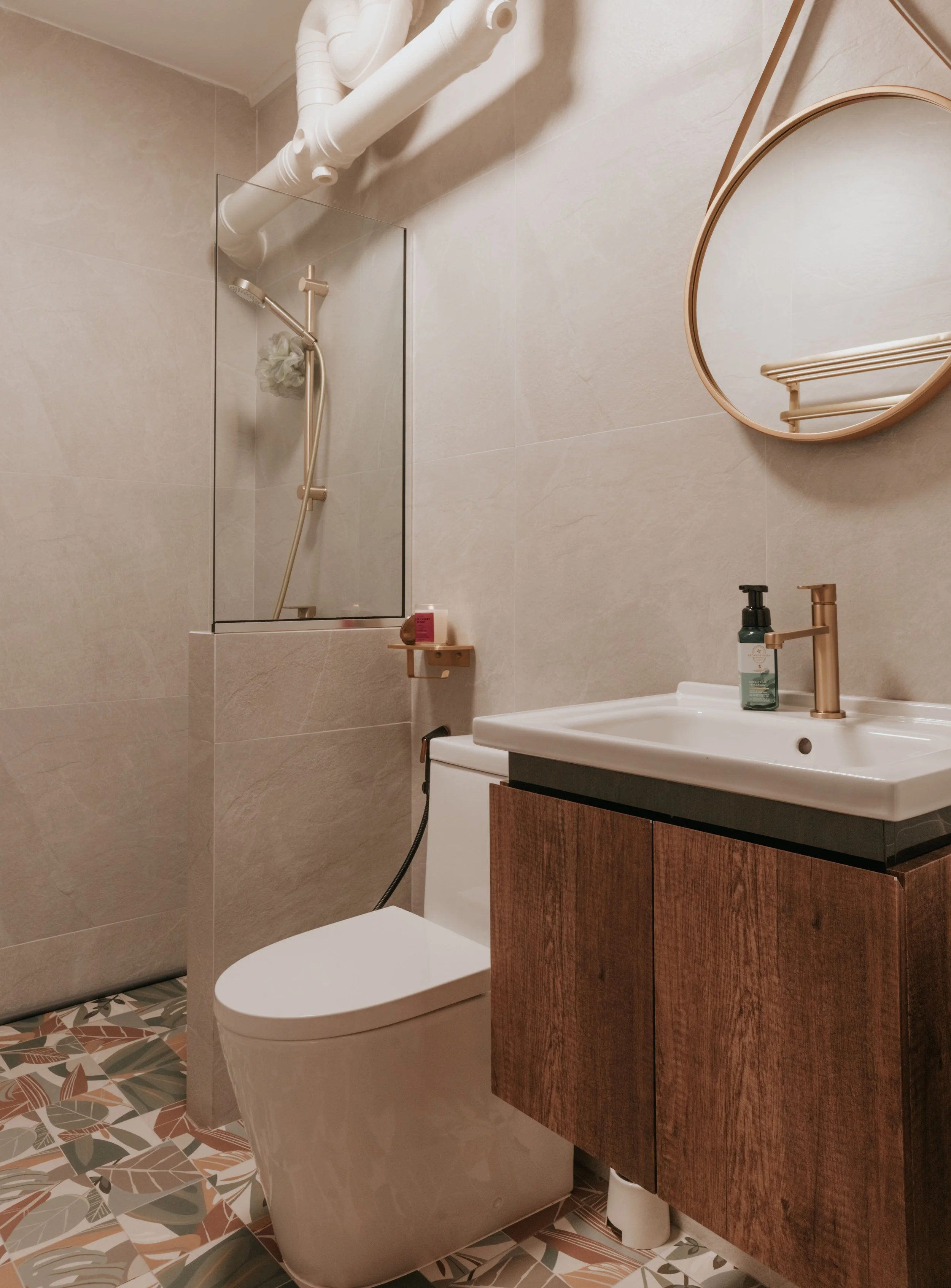 Modern bathroom with a walk-in shower, toilet, and a wooden vanity with a sink, a round wall mirror, and patterned floor tiles.