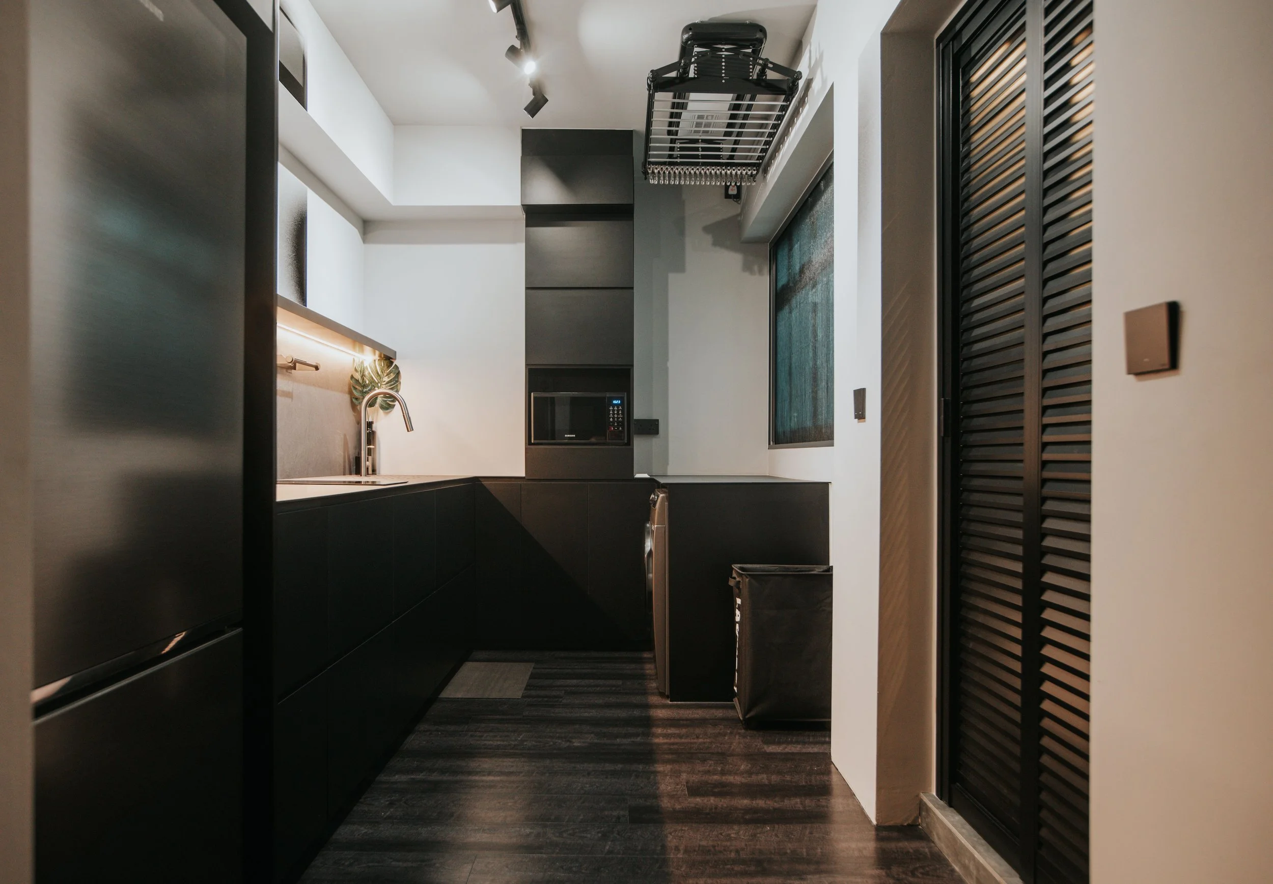 Modern kitchen with black cabinets, a built-in microwave, a small sink with a faucet, an overhead dish rack, and dark wood flooring.