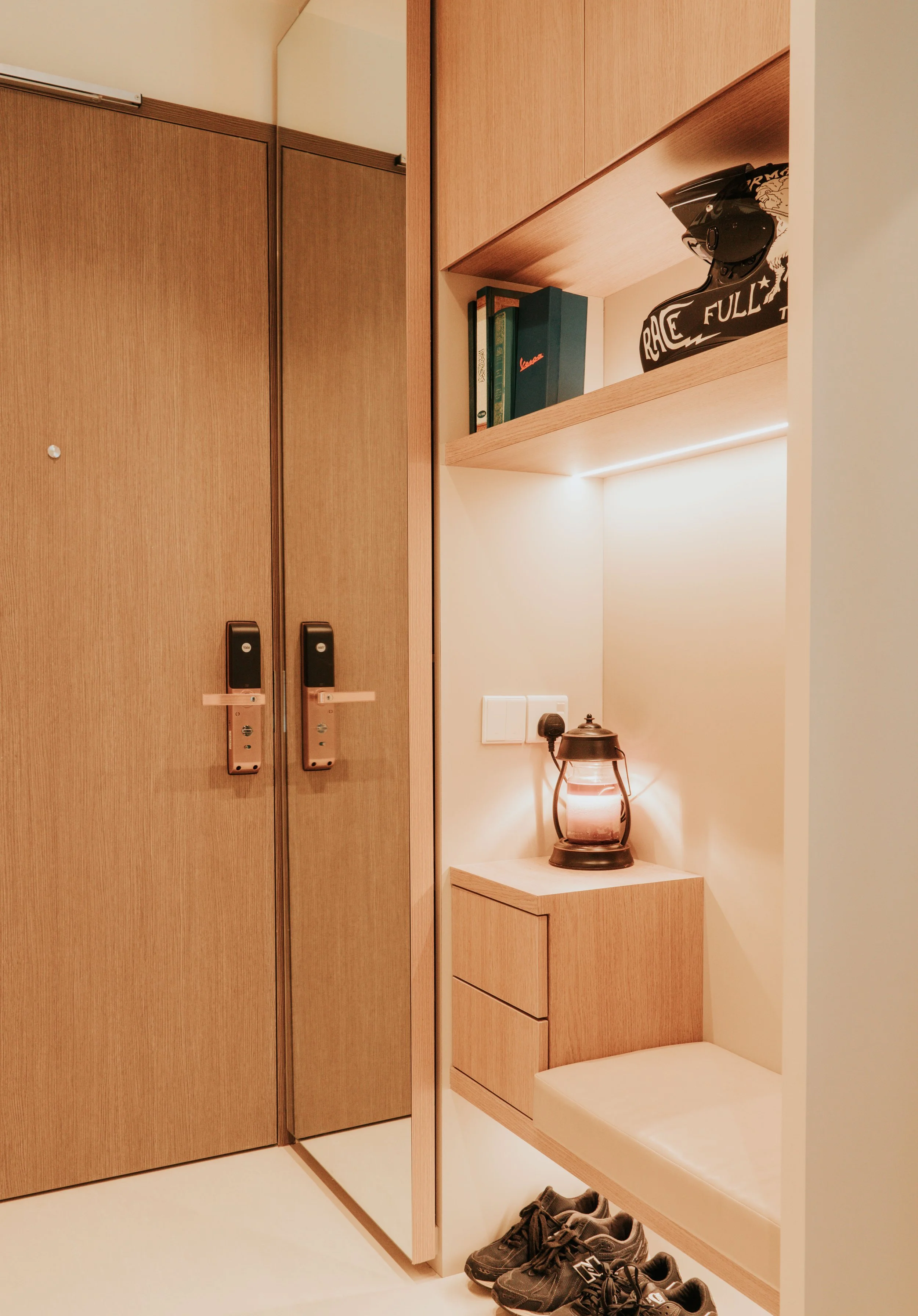 Wooden closet with two closed doors next to a nook with drawers, a lantern, and a row of sneakers on the floor.