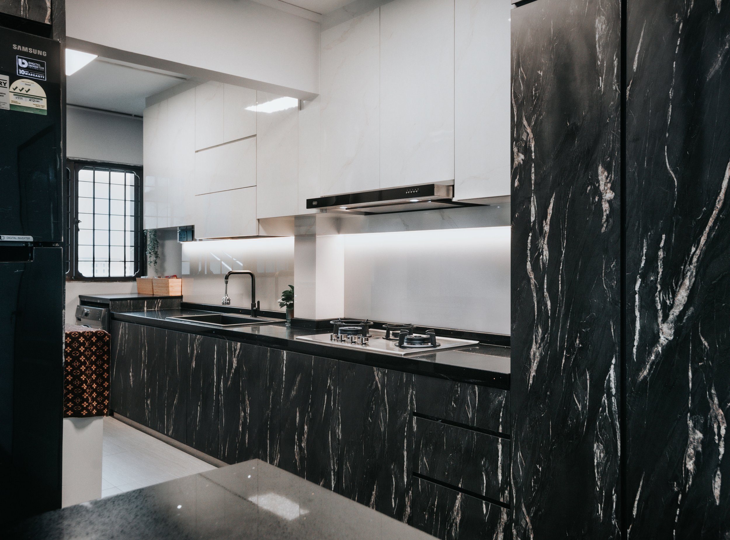 Sleek modern kitchen featuring black marble countertops and white cabinetry, illuminated by under-cabinet lighting.