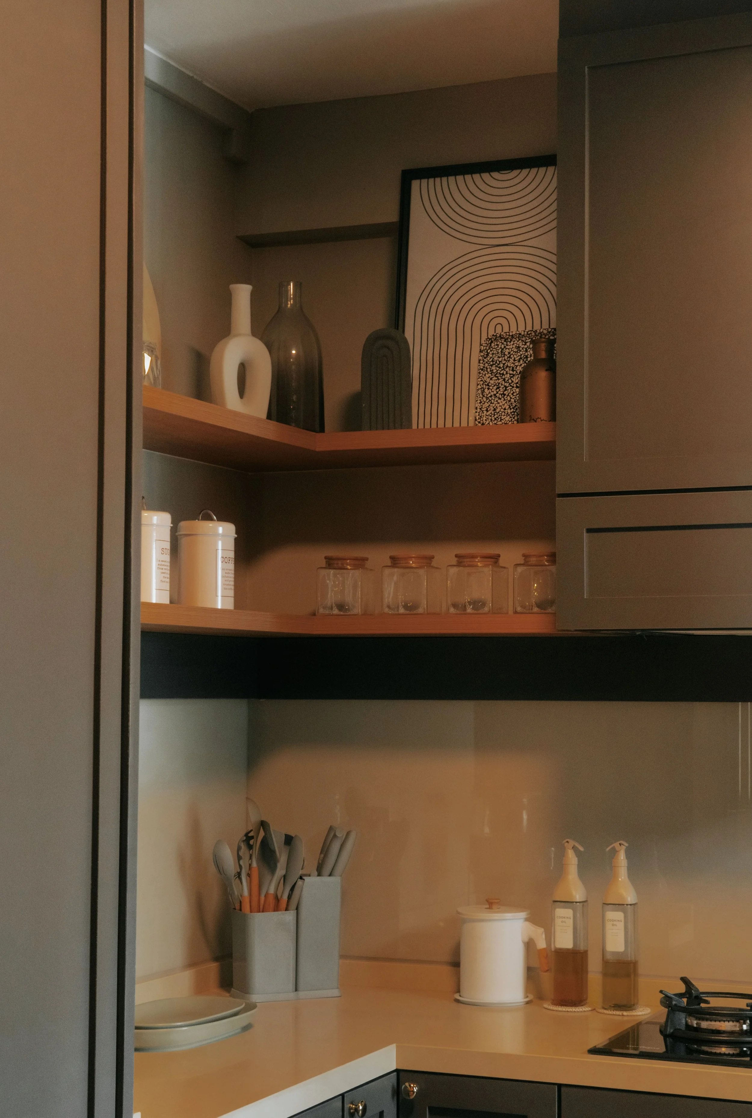 Open kitchen cabinet with shelves containing decorative vases, framed artwork, glass jars, and kitchen utensils on the counter.