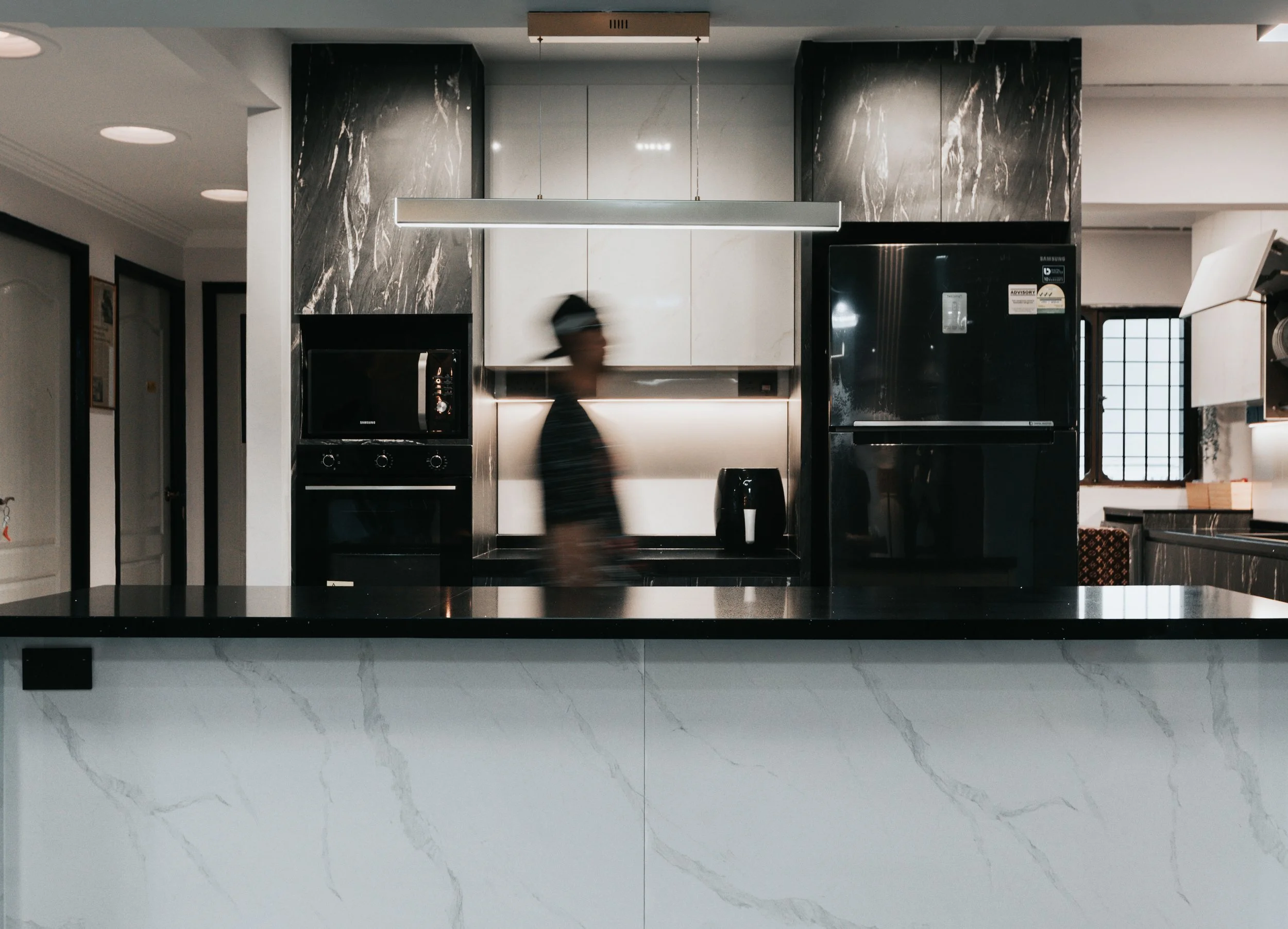 A person blurred in motion in a sleek modern kitchen with a marble island and black appliances.