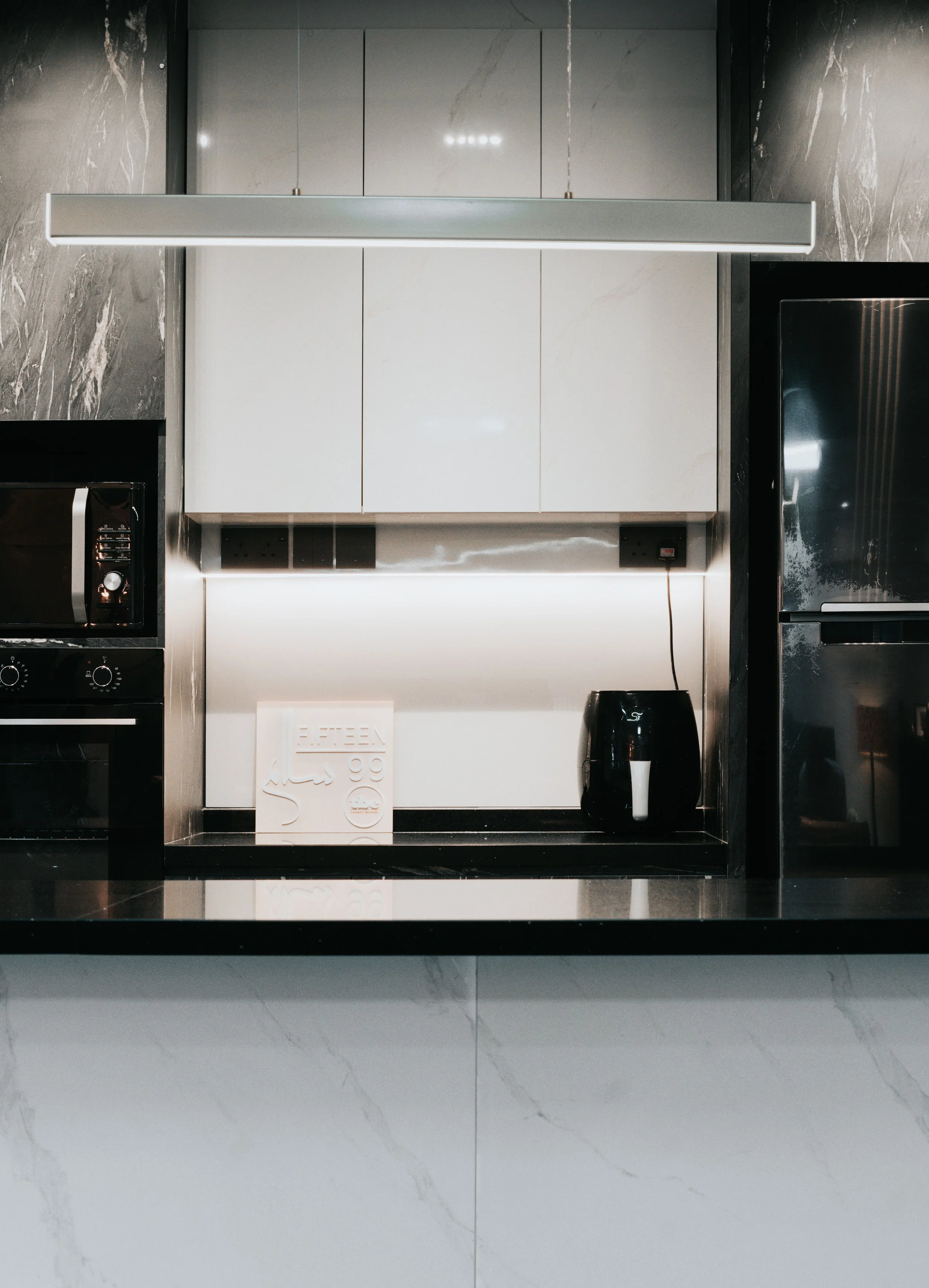Sleek modern kitchen featuring black marble countertop and stainless steel appliances under a bright overhead light.