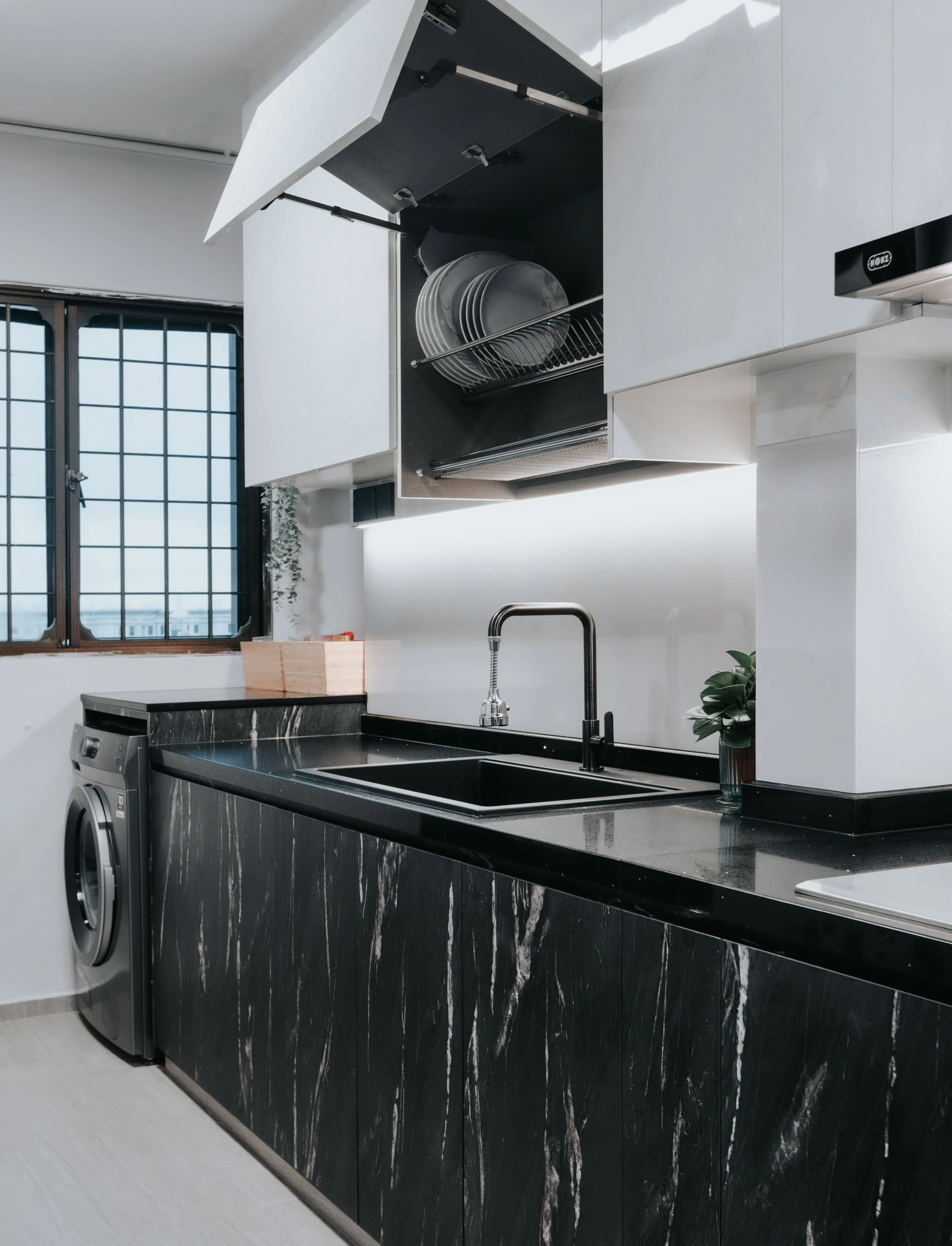 A sleek modern kitchen featuring a black countertop and open cabinet displaying white dishes.
