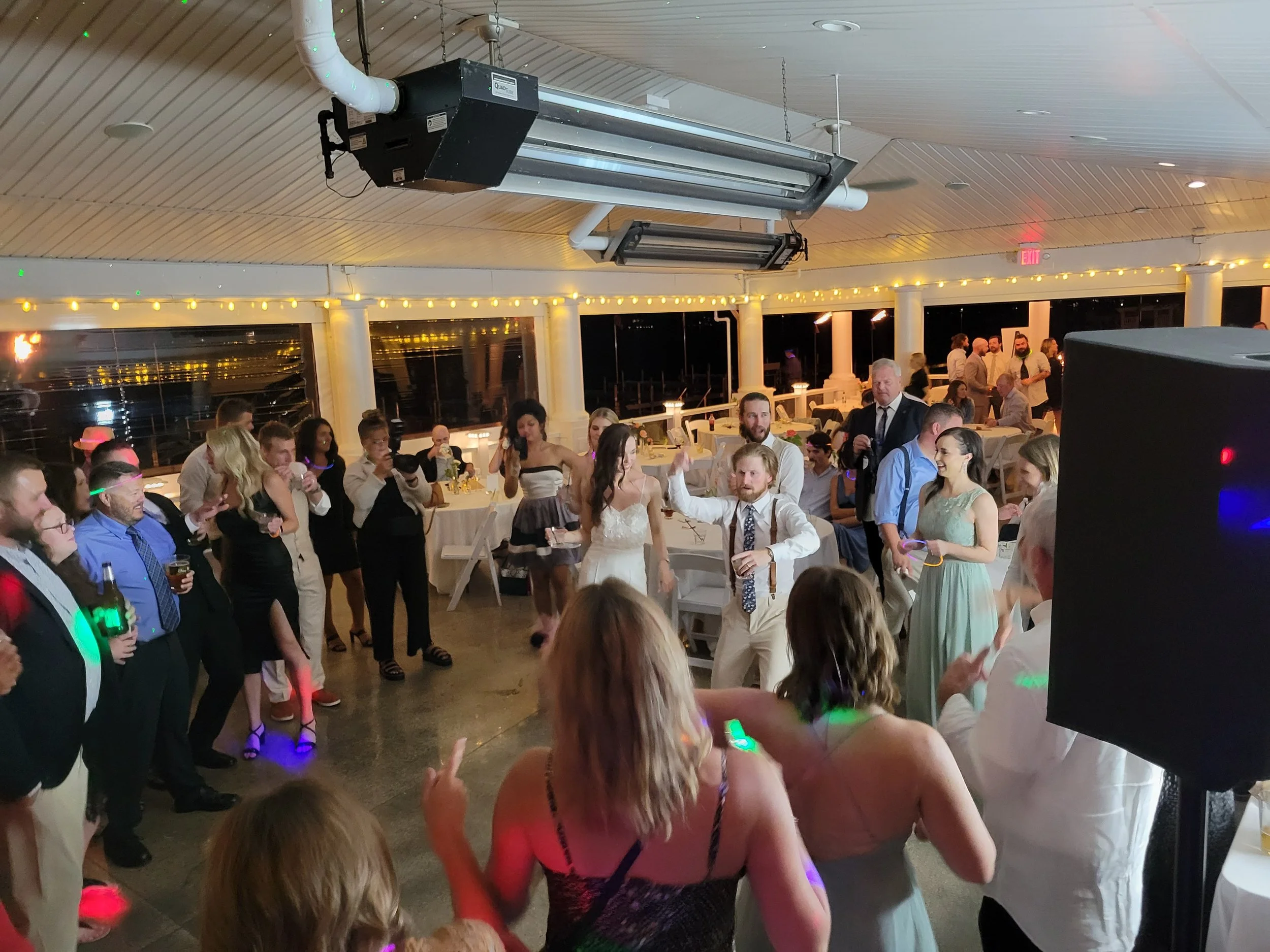 Guests dancing and socializing at a wedding reception on a decorated outdoor deck at night.