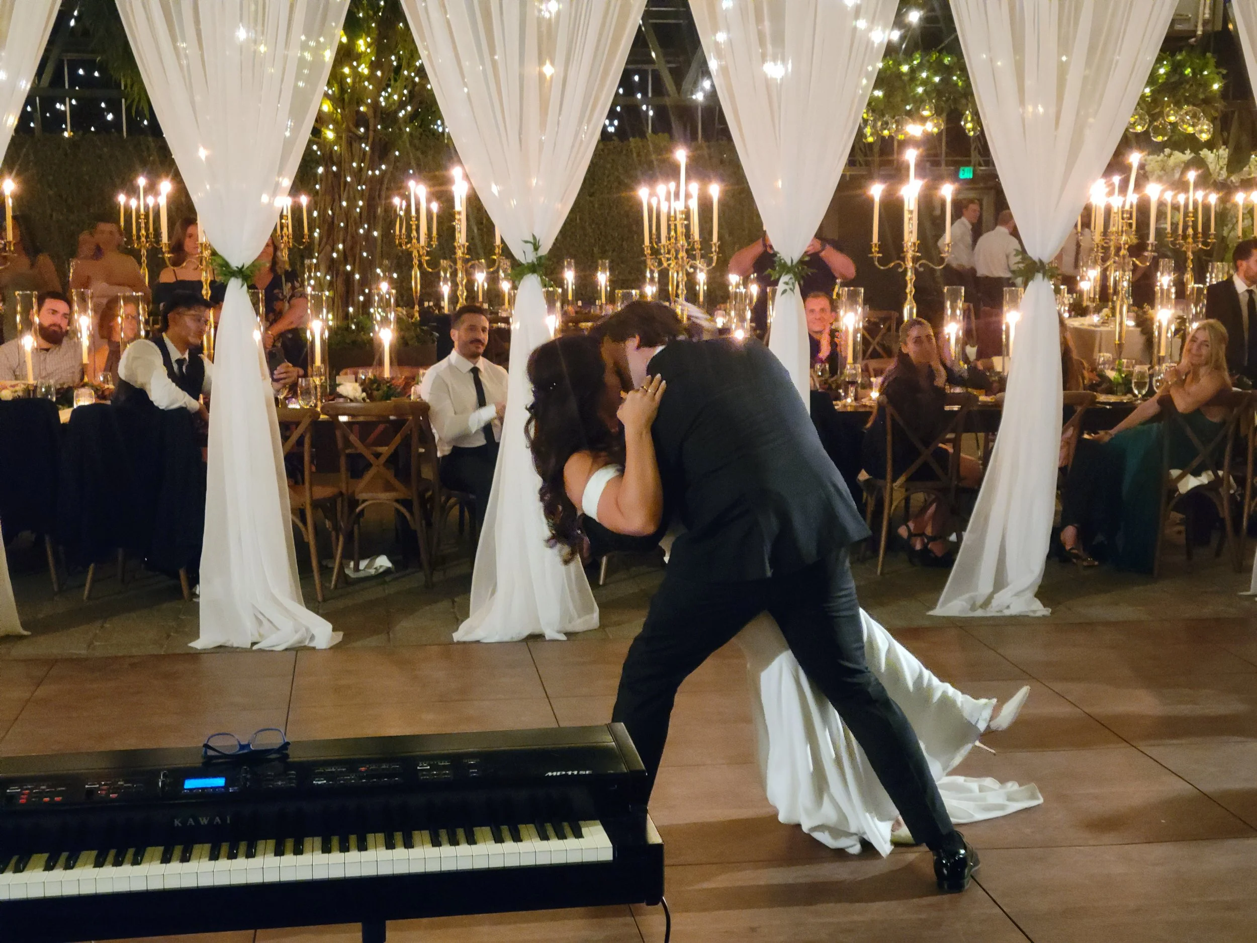 A newlywed couple sharing a dance at their wedding reception with guests seated at decorated tables in the background