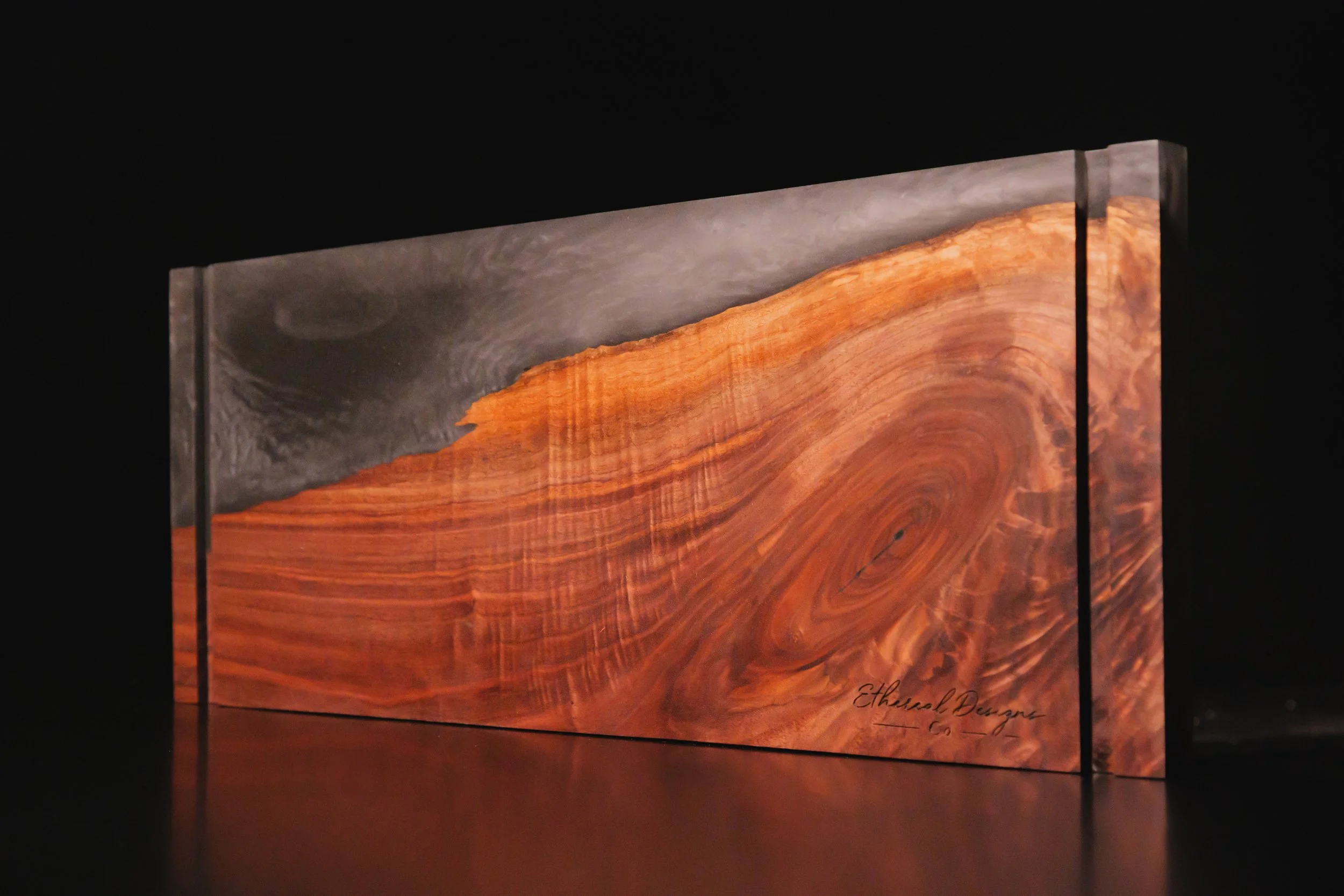 A close-up photograph of a wooden plaque with a metallic border and a signature at the bottom right corner titled 'Ethereal Designs Co.'.