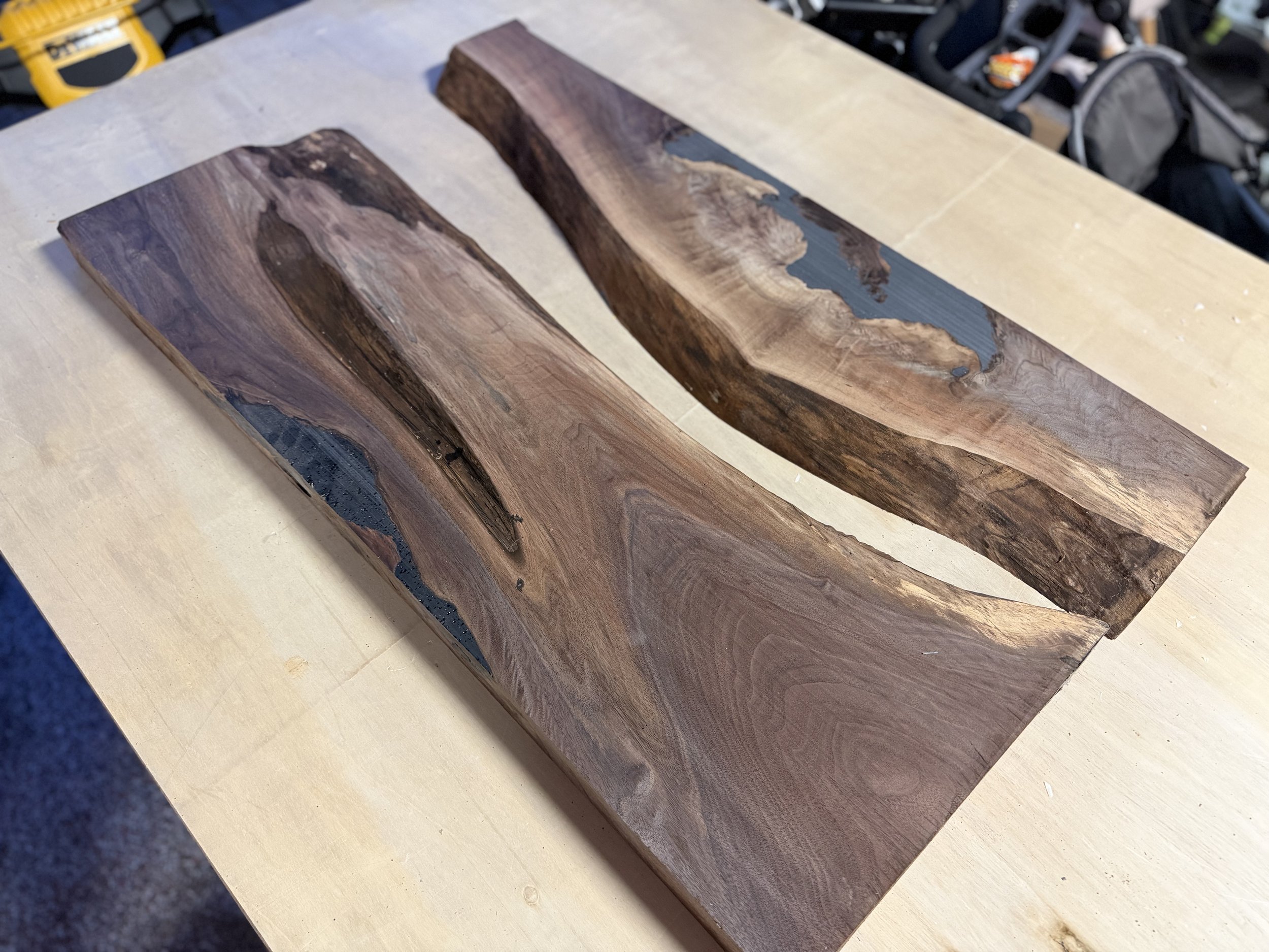 Two wooden slabs with dark resin filling natural edges resting on a light-colored table