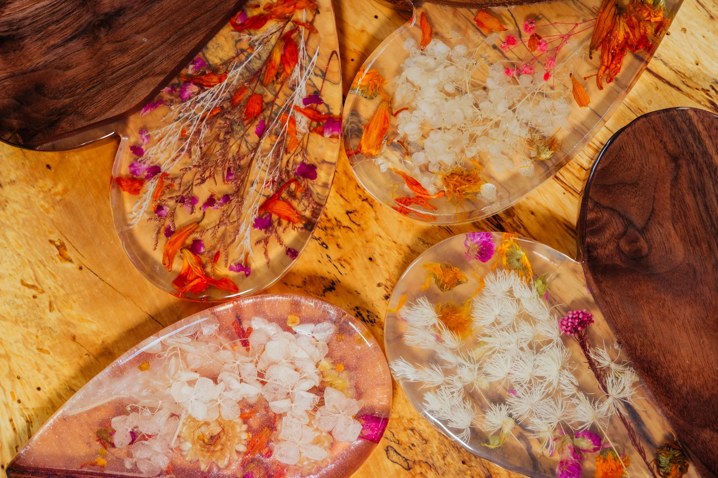 Multiple clear resin dishes containing dried flowers and botanical materials on a wooden surface.