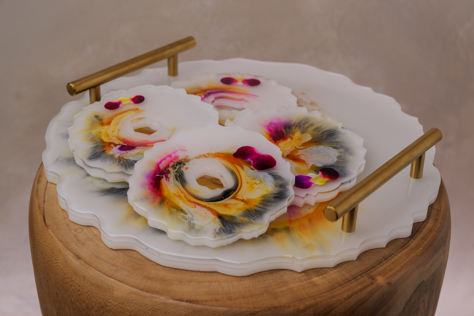Decorative resin coasters with colorful swirling patterns and dried flower petals, displayed on a round wooden stand with brass handles.