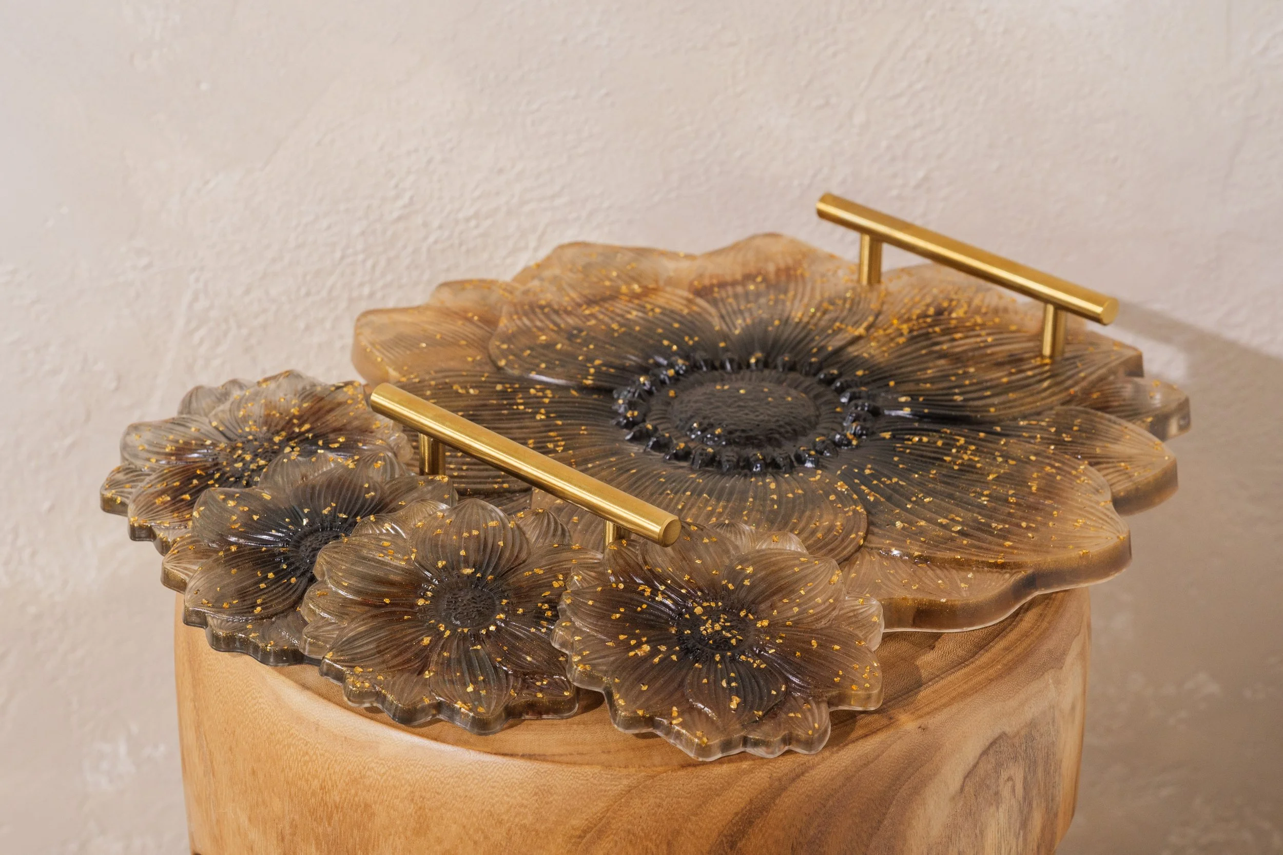 Decorative wooden table with gold accents, designed to resemble large flowers with petal-like layers, placed on a wooden pedestal against a plain white wall.