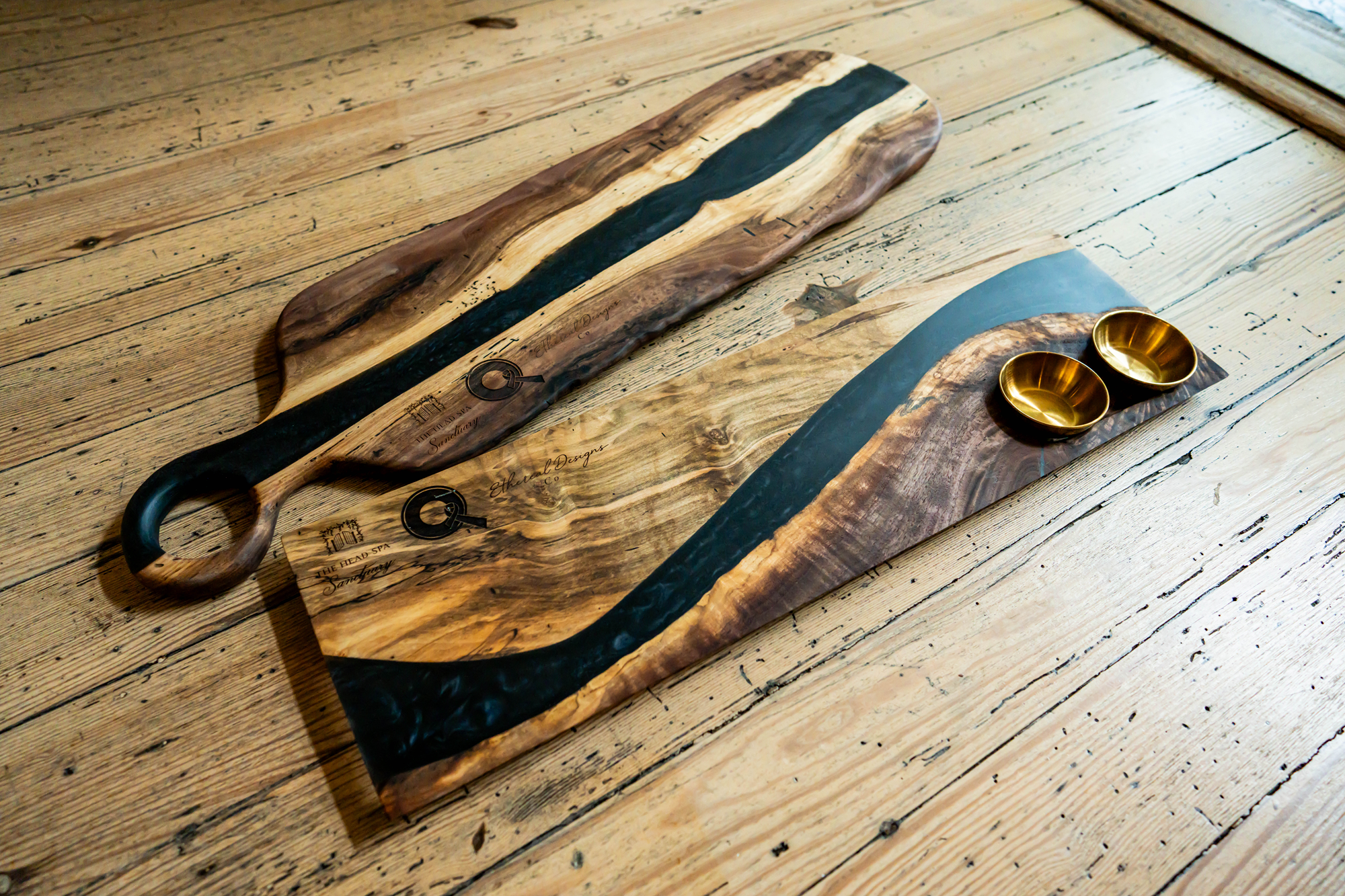 A long wooden serving board with a black stripe in the middle, placed on a wooden table. Two small gold bowls are on a separate small wooden board with a similar design.