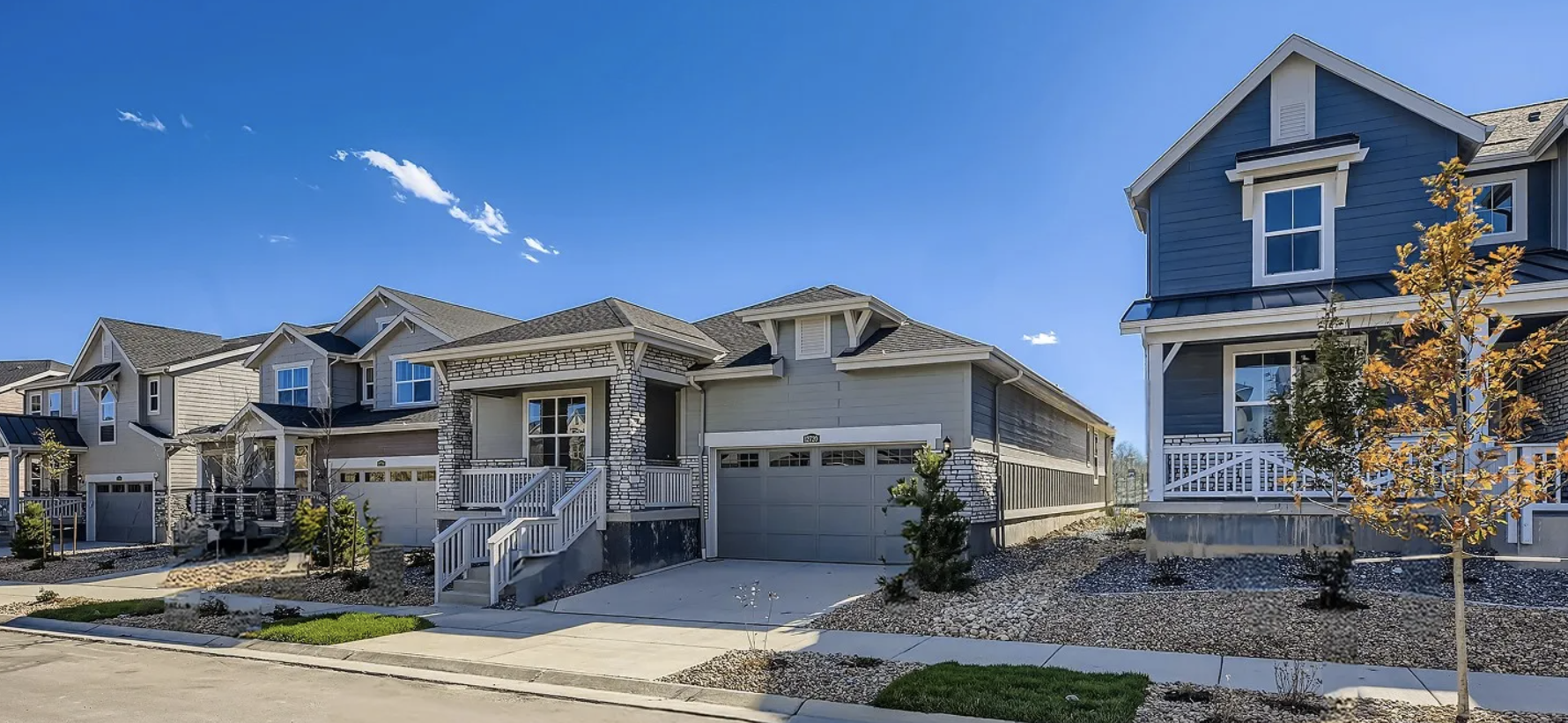 A row of modern suburban houses with garages, small front yards, and a clear blue sky.