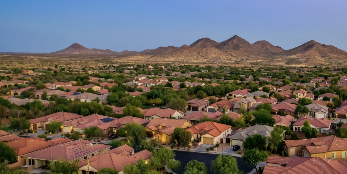 Aerial view of a suburban neighborhood with many houses and streets, with mountains visible in the background during dusk.