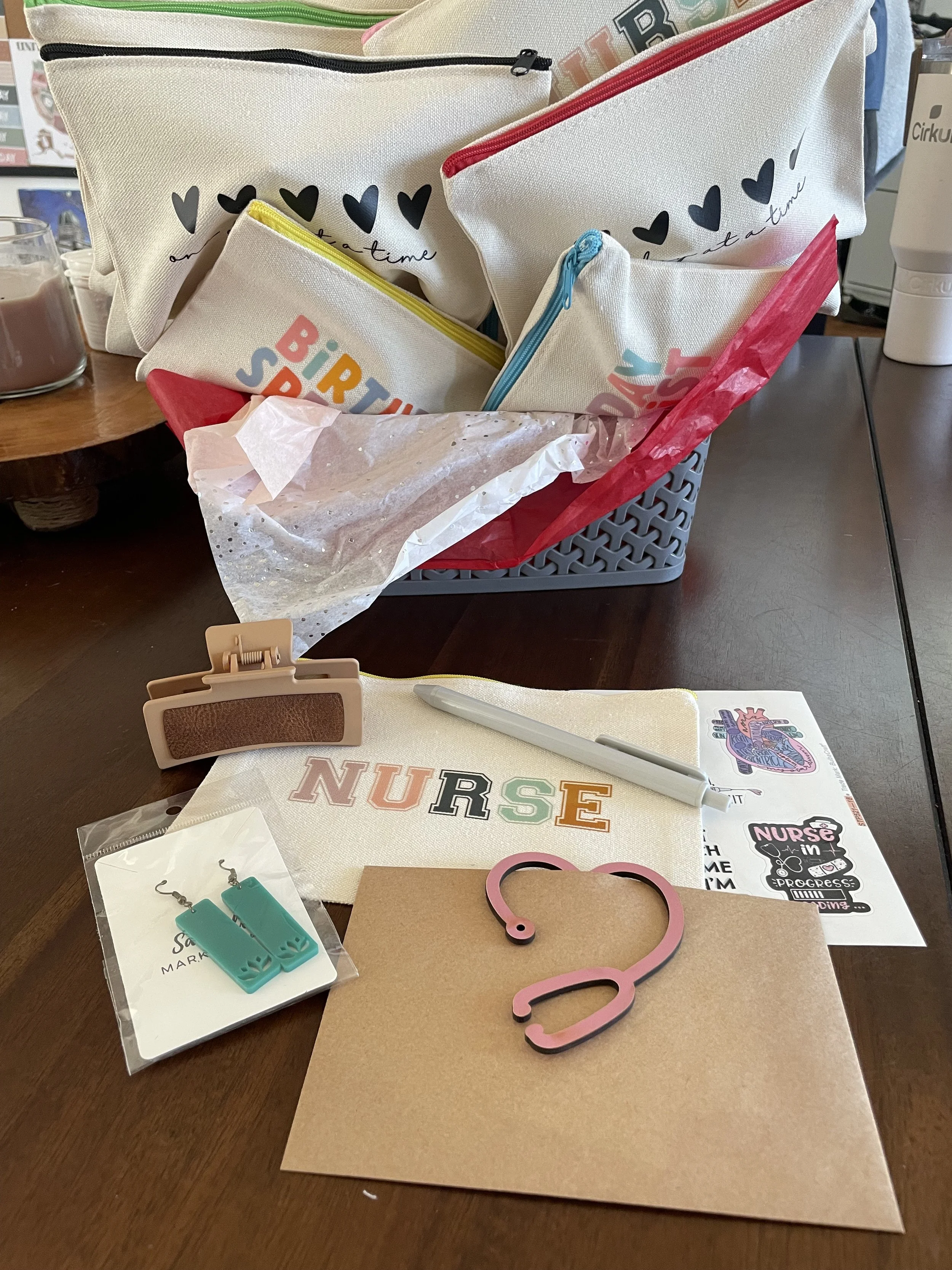 A collection of nursing-themed craft supplies on a wooden table, including fabric pouches with heart and rainbow designs, a pink question mark, teal medical gloves, and a paper with the word 'NURSE' in colorful letters.