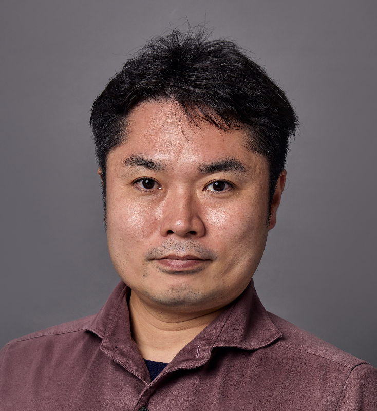 A man with short black hair and light skin looking directly at the camera against a gray background.