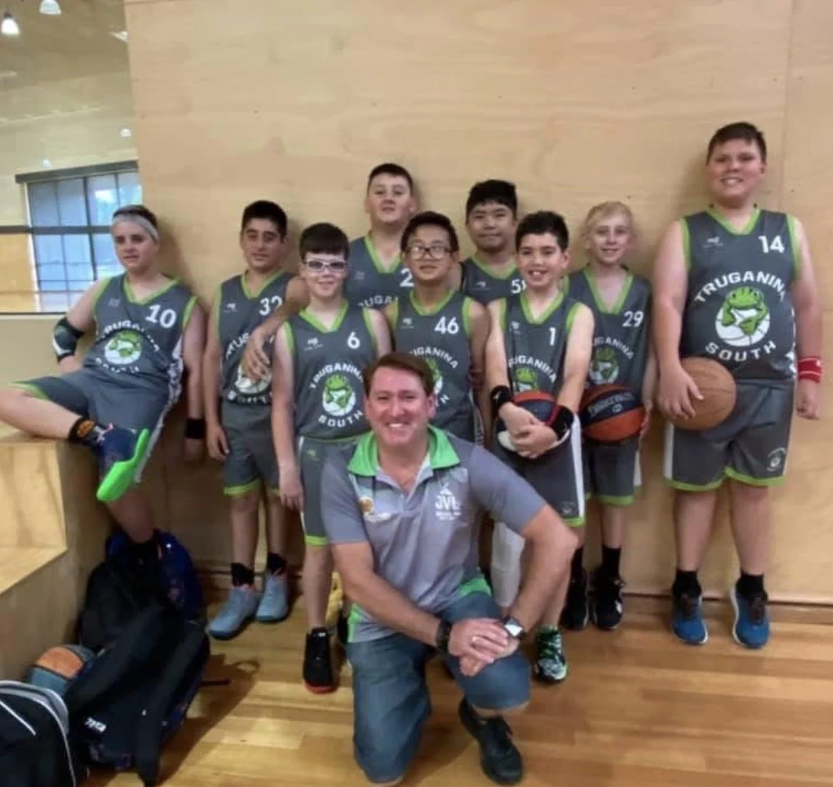 A youth basketball team with their coach in a gym, wearing gray and green uniforms with 'Truganina South' logo, posing for a team photo.