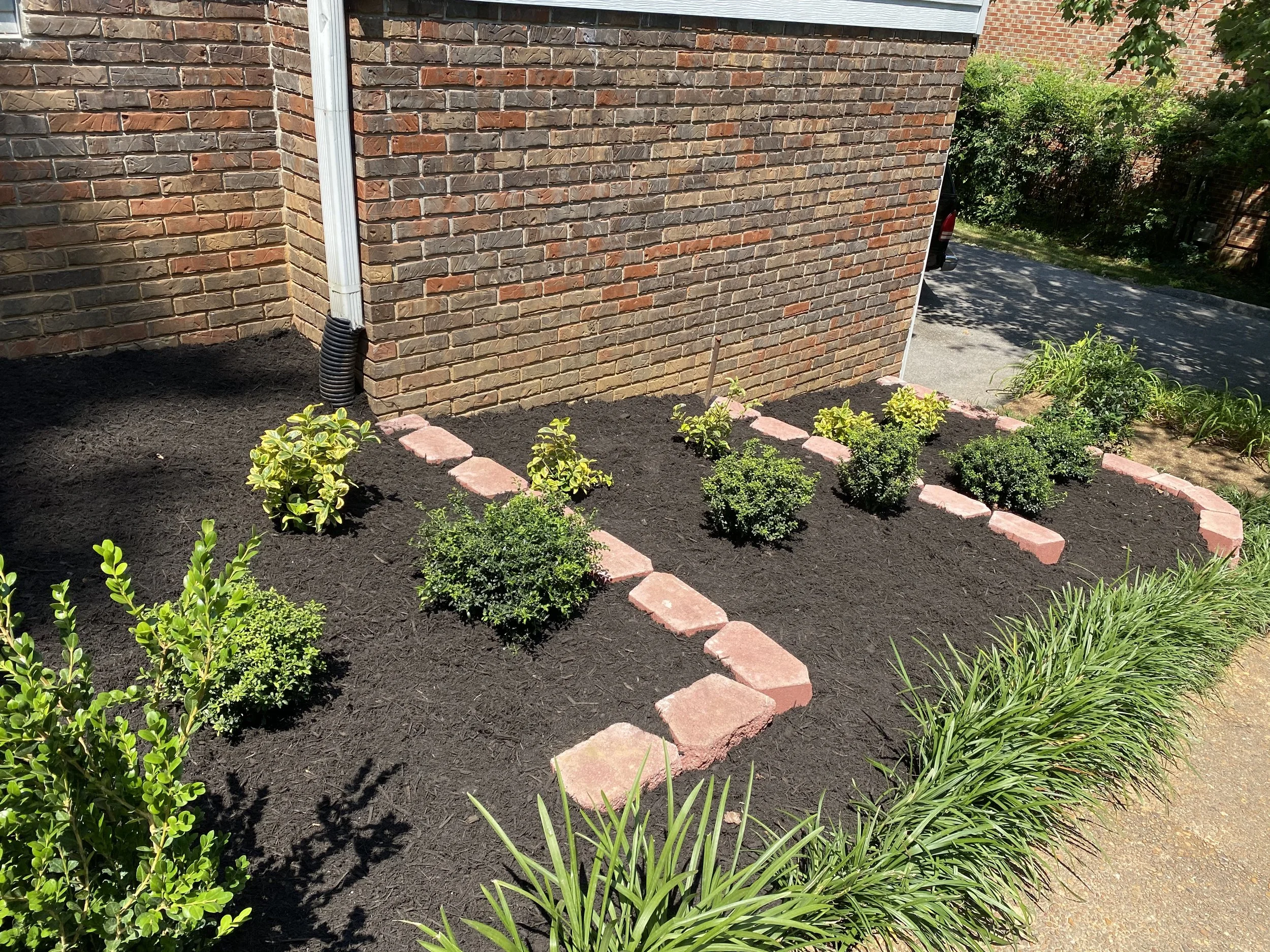 A gated brick wall with a flower bed in front, featuring small bushes and mulch, bordered with pink bricks.