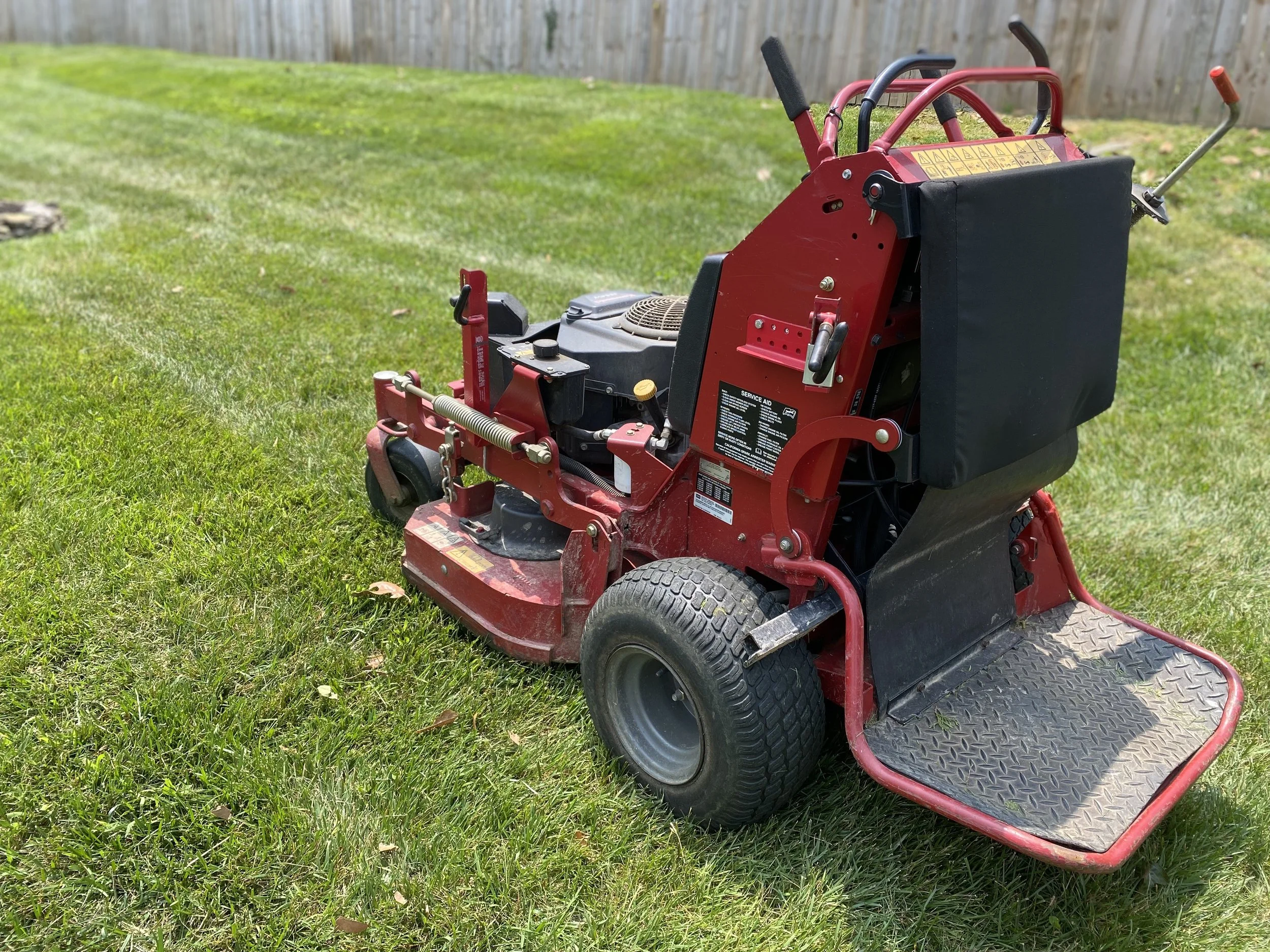 Red turf cutting machine on a grassy lawn with a wooden fence in the background.