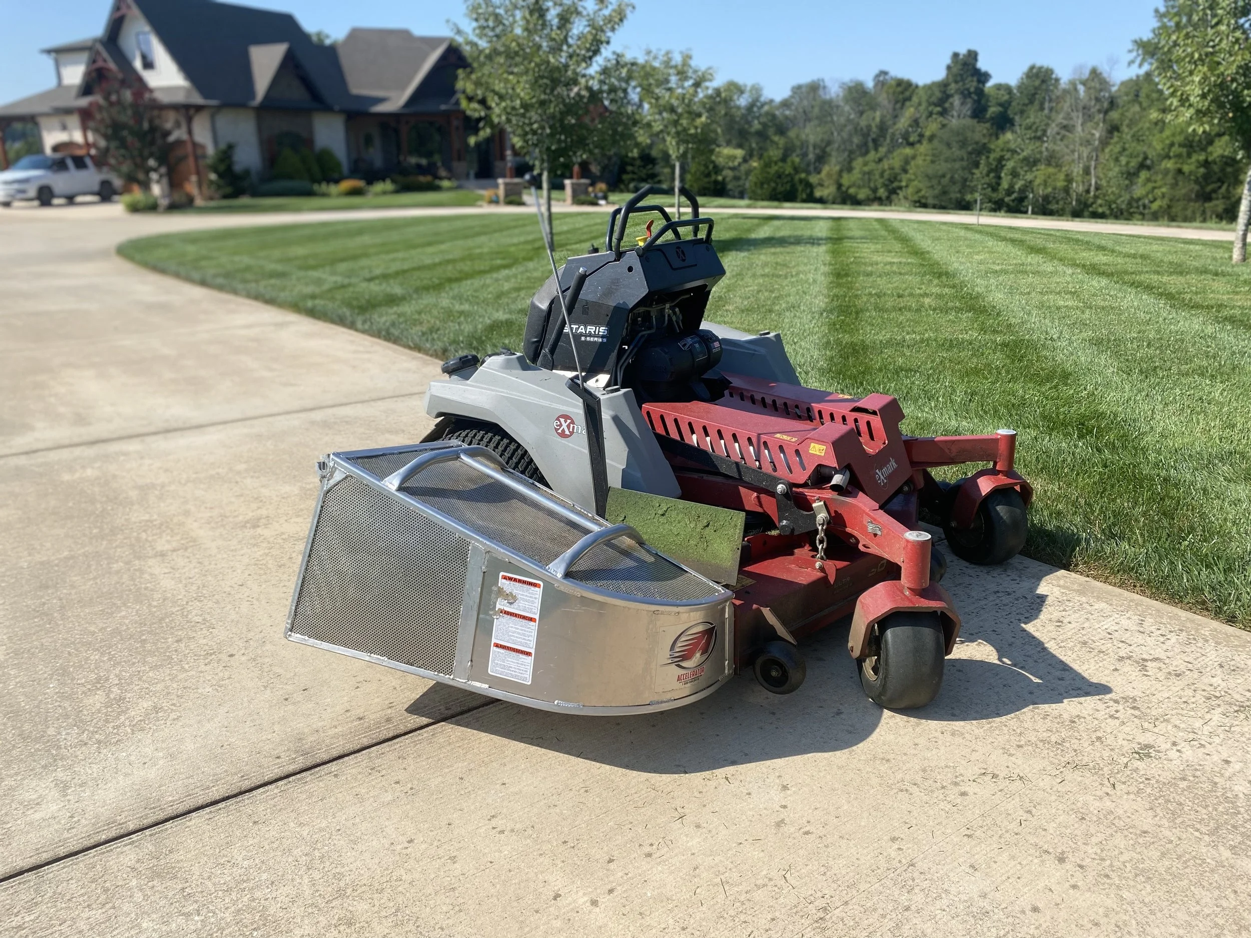 Lawn mowing machine on a driveway with a house and green lawn in the background.