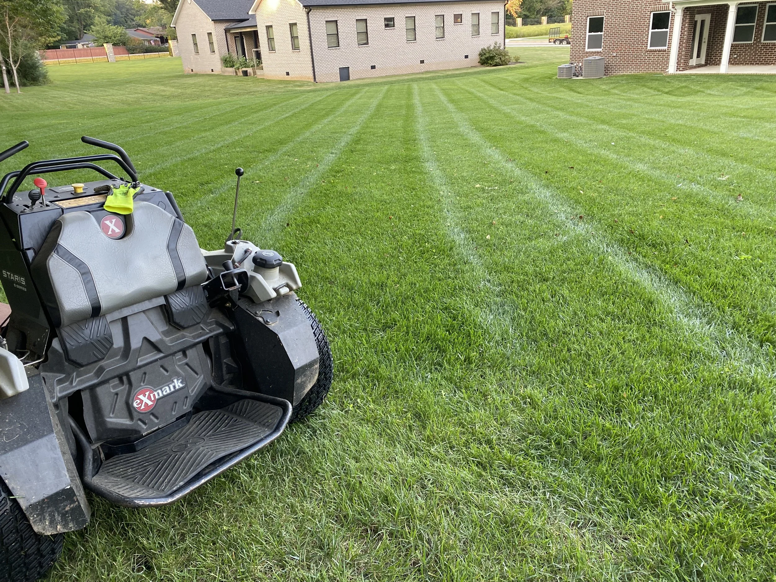 A lawn mower parked on a well-maintained grassy lawn with houses in the background.