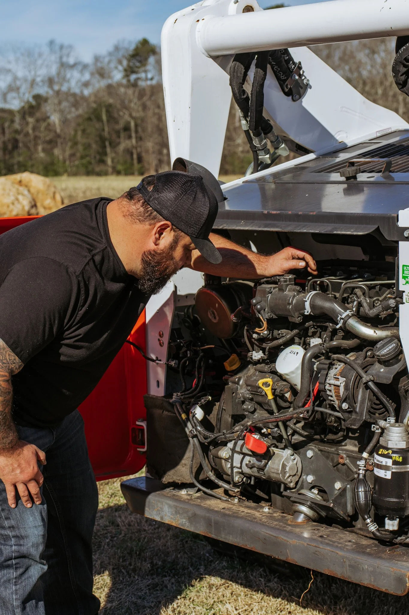 Man inspecting a vehicle engine outdoors on a sunny day.